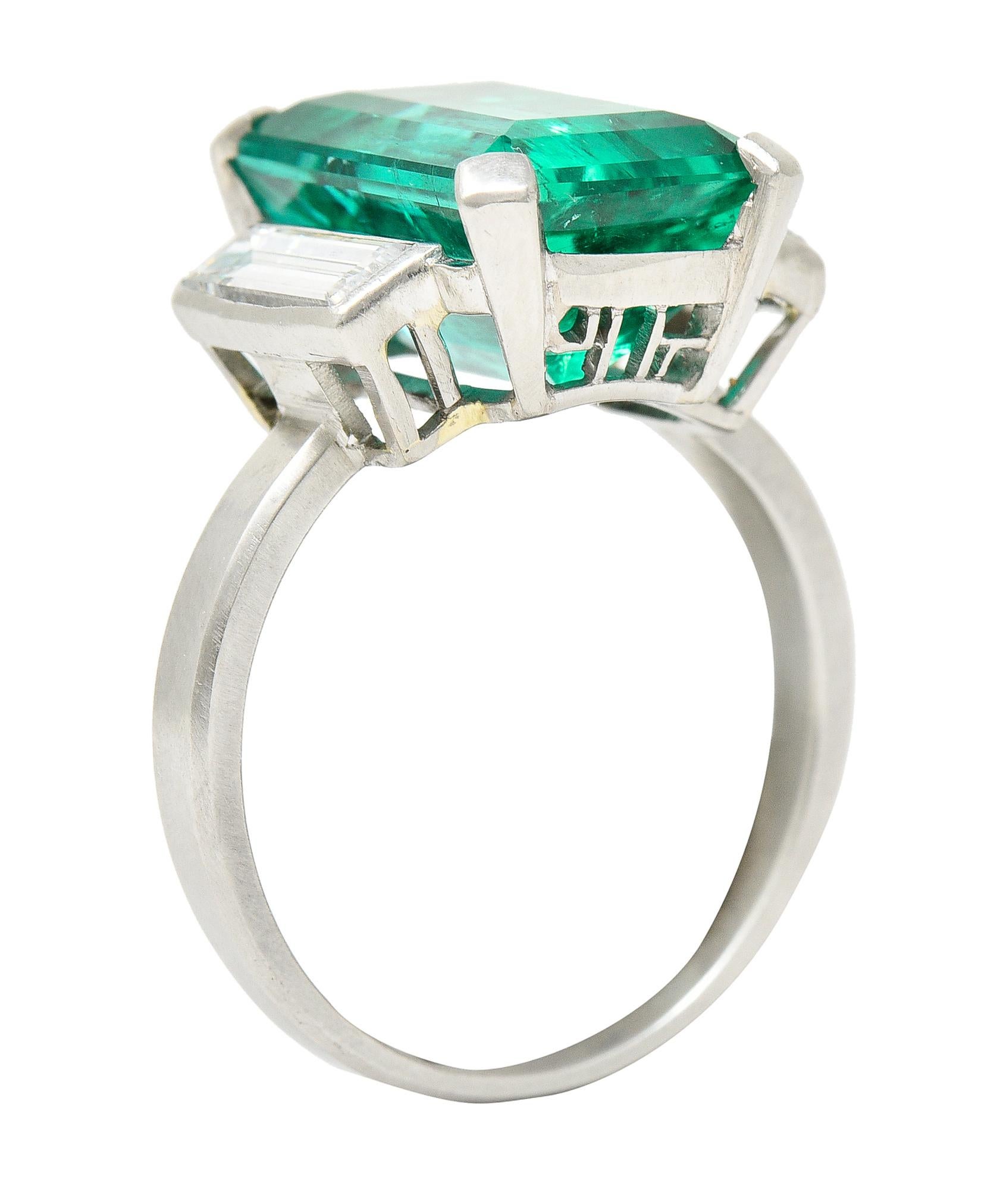 Centering an emerald cut emerald weighing approximately 5.78 carats total - Columbian in origin. Transparent medium blueish green in color with natural inclusions - moderate clarity enhancement F2. Prong set in a stylized pierced modernist cubist