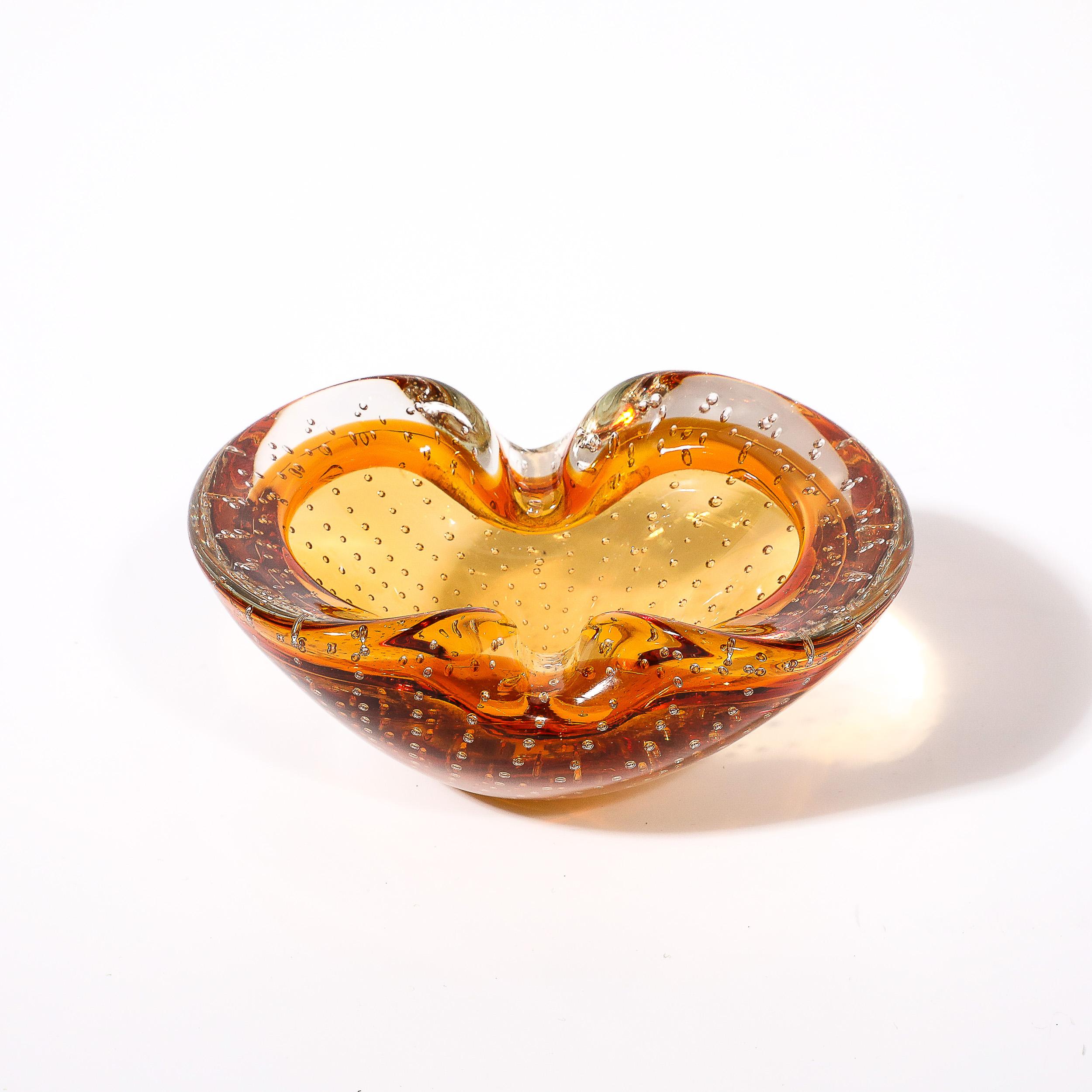 This elegant and sculptural Mid-Century Modernist Hand-Blown Murano Glass Dish with Bullicante Detailing in Amber originates from Italy, Circa 1950. Features an hourglass silhouette when viewed from above achieved by two subtle lips drawn towards