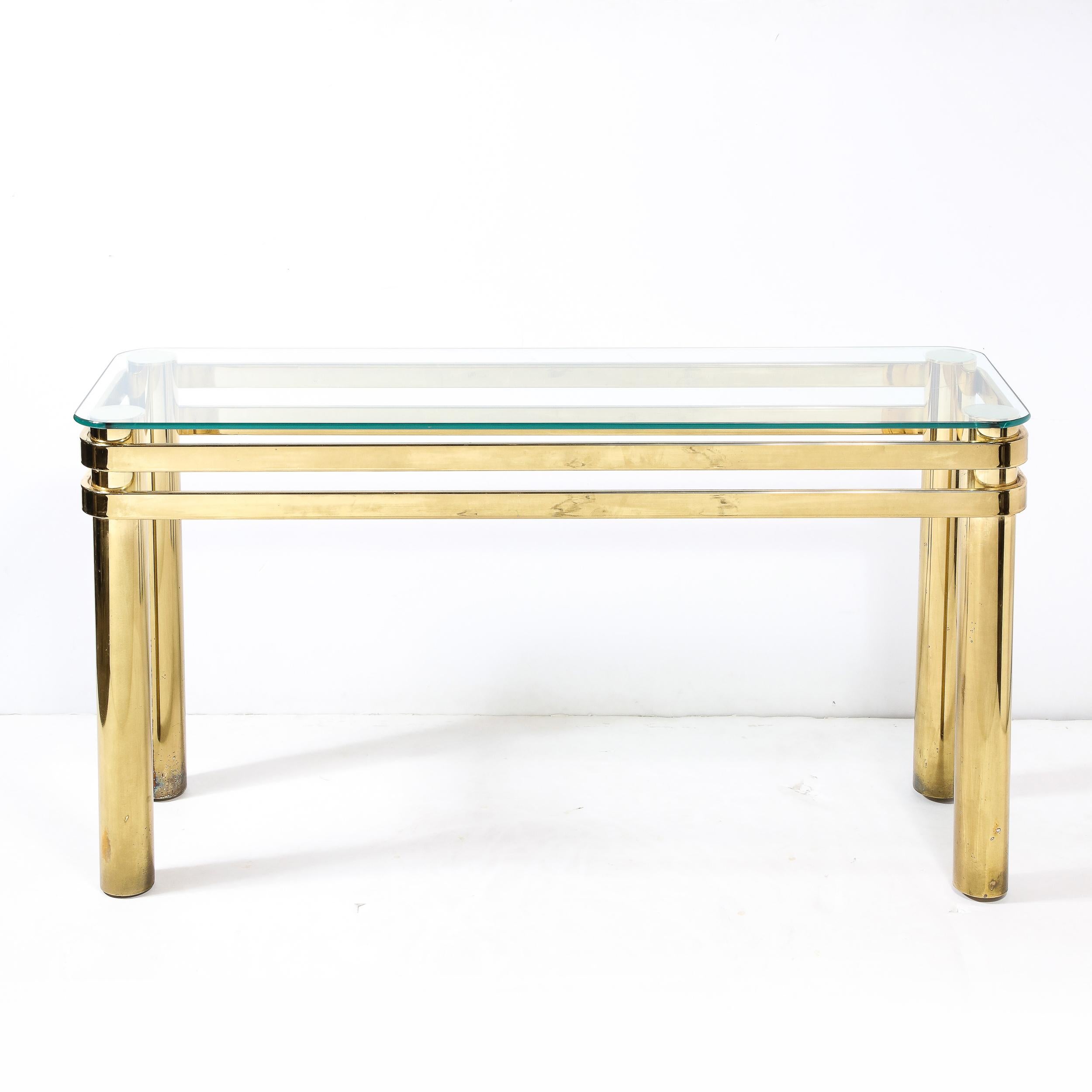 Cette étonnante table console en laiton bagué, de style moderniste du milieu du siècle, avec des supports à colonnes, est fabriquée aux États-Unis, vers 1970. Une belle table console avec un plateau en verre transparent, rectangulaire avec des coins