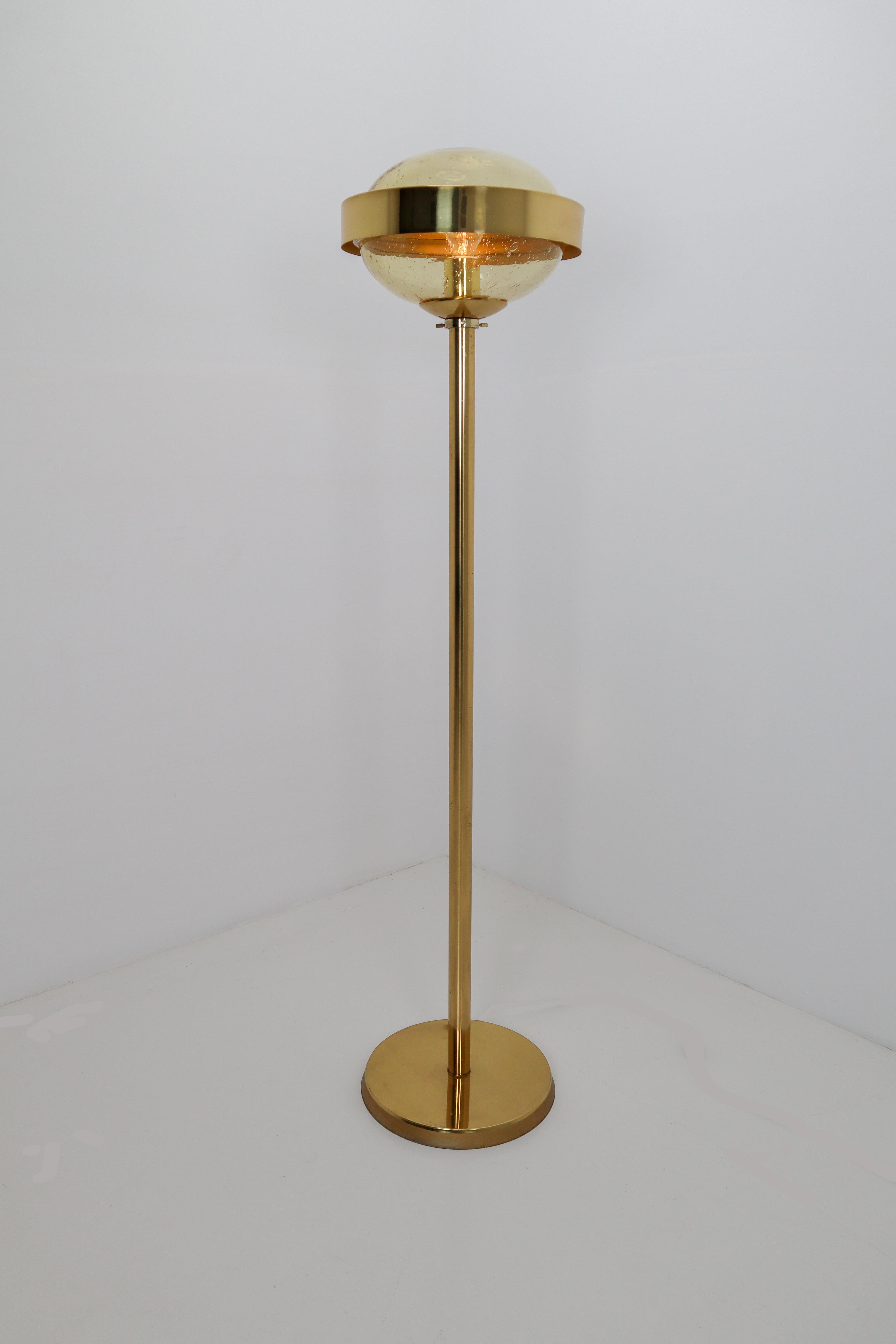 Mid-Century Modernist brass and hand-blowed glass floor lamp, 1960s. The handblown glass globe have a amber tint to them and contain air bubbles of varying sizes and density that create a wonderful light effect. This floor lamp will contribute to a