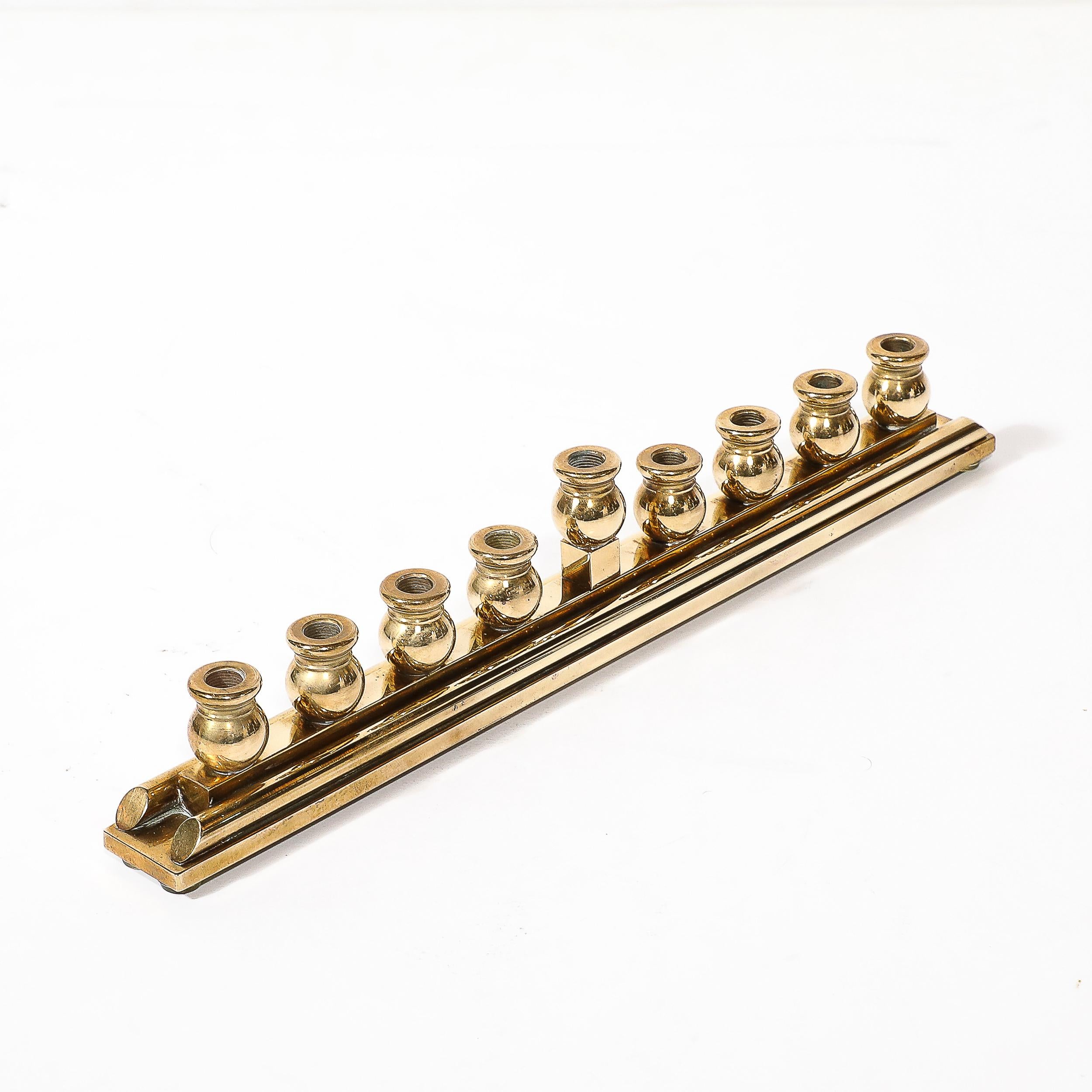 This sleek and elegant Mid-Century Modernist Brass Menorah signed Morningstar Metalworks origiantes from the United States, C. 1998. This piece features a well balanced rectilinear base with nine rounded classically formed lamps, the center of which