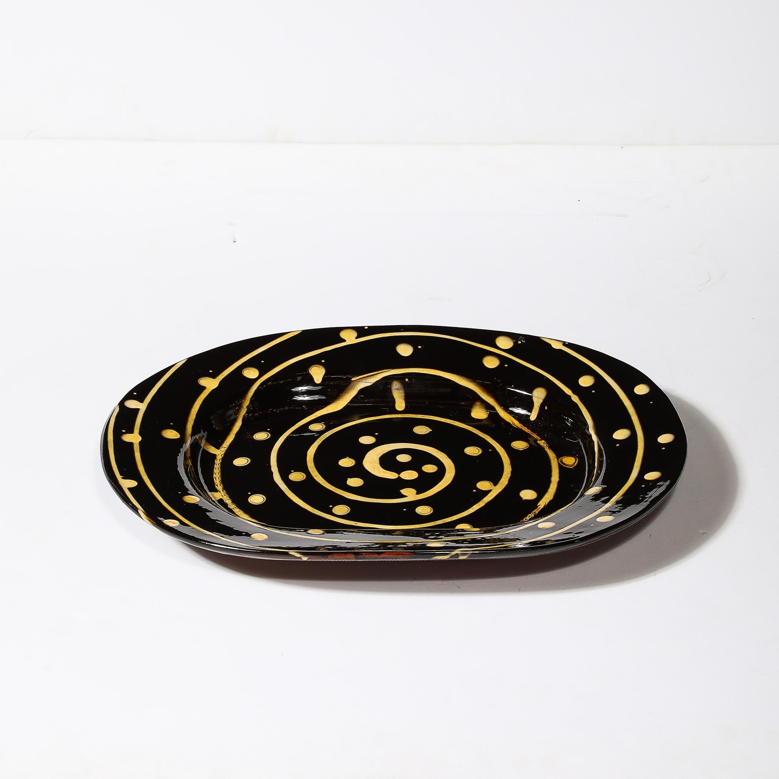 Ce plateau de service en céramique moderniste du milieu du siècle, avec spirale et points jaunes, provient des États-Unis, vers 1980. Elle présente une forme ovale avec un rebord surélevé et des motifs glacés graphiques noirs et jaunes qui attirent