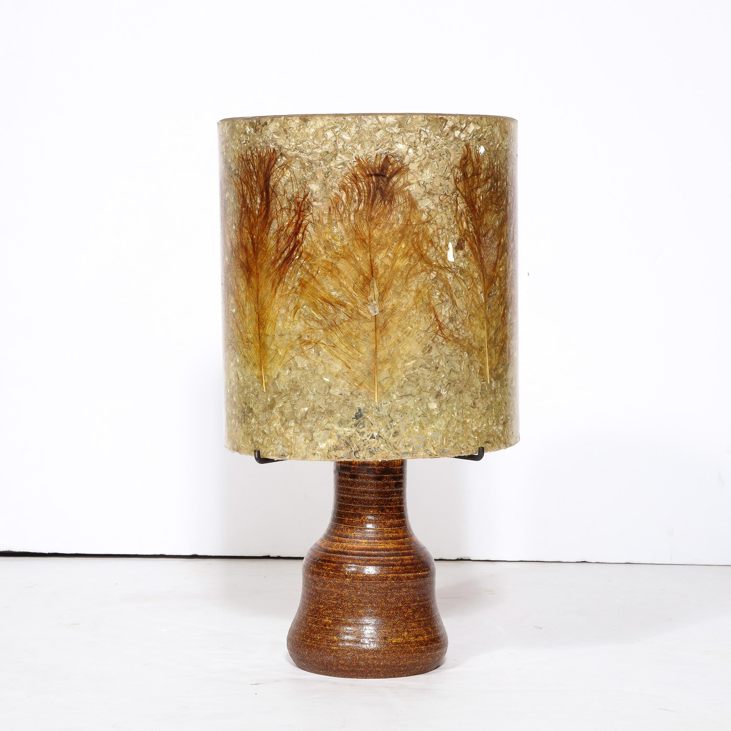 This sophisticated Mid-Century Modern table lamp was realized in France circa 1960. It features an sculptural undulating base in a rich iron oxide hue with subtle horizontal striations. The exquisite shade of the piece is composed of richly textured