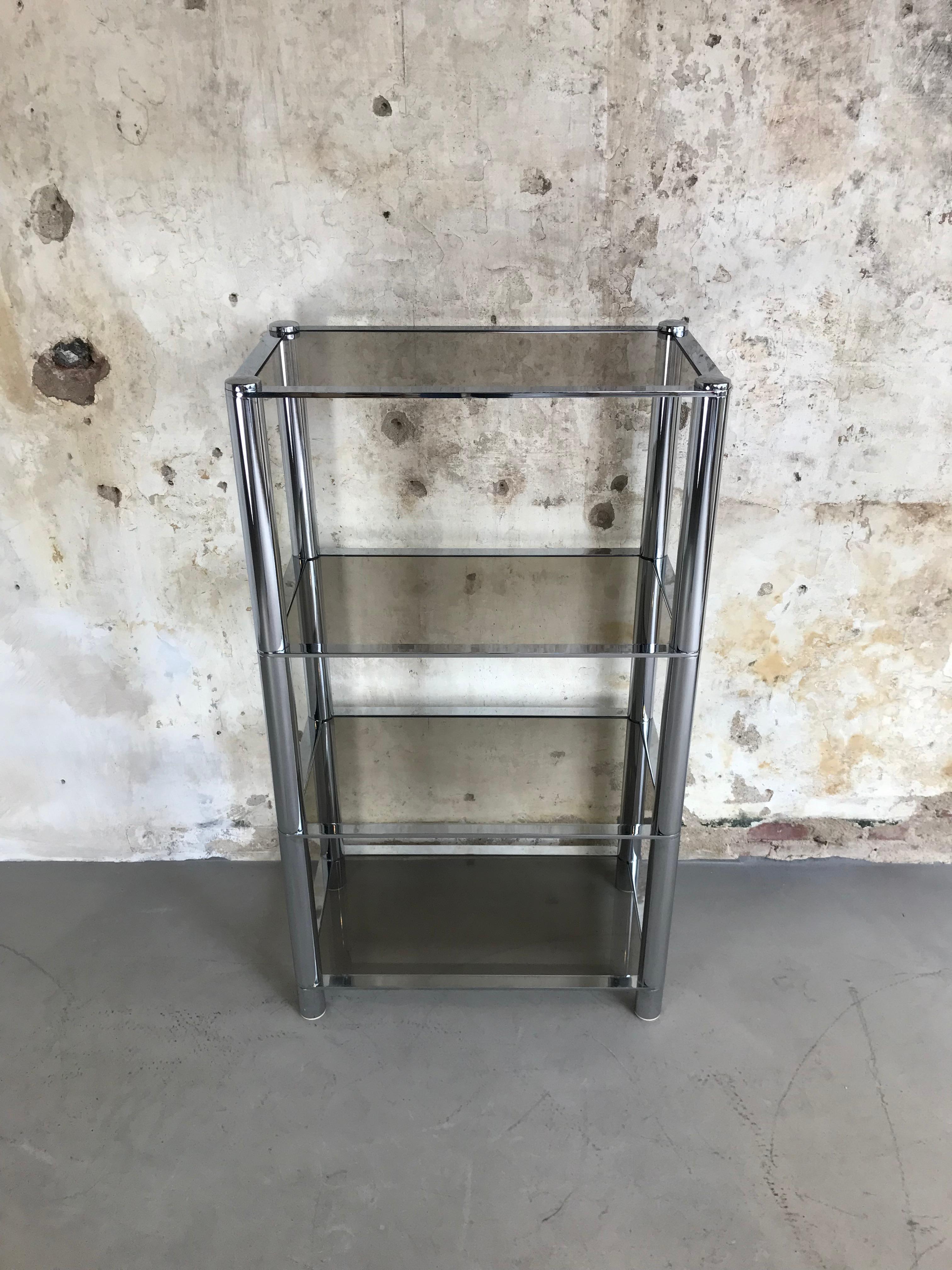Amazing chrome tubular étagère in the style of Milo Baughman. Composed of four smoked glass shelves in a glimmering chrome body, this étagère offers an elegant way to present everything that your heart desires. 
This piece is in excellent vintage