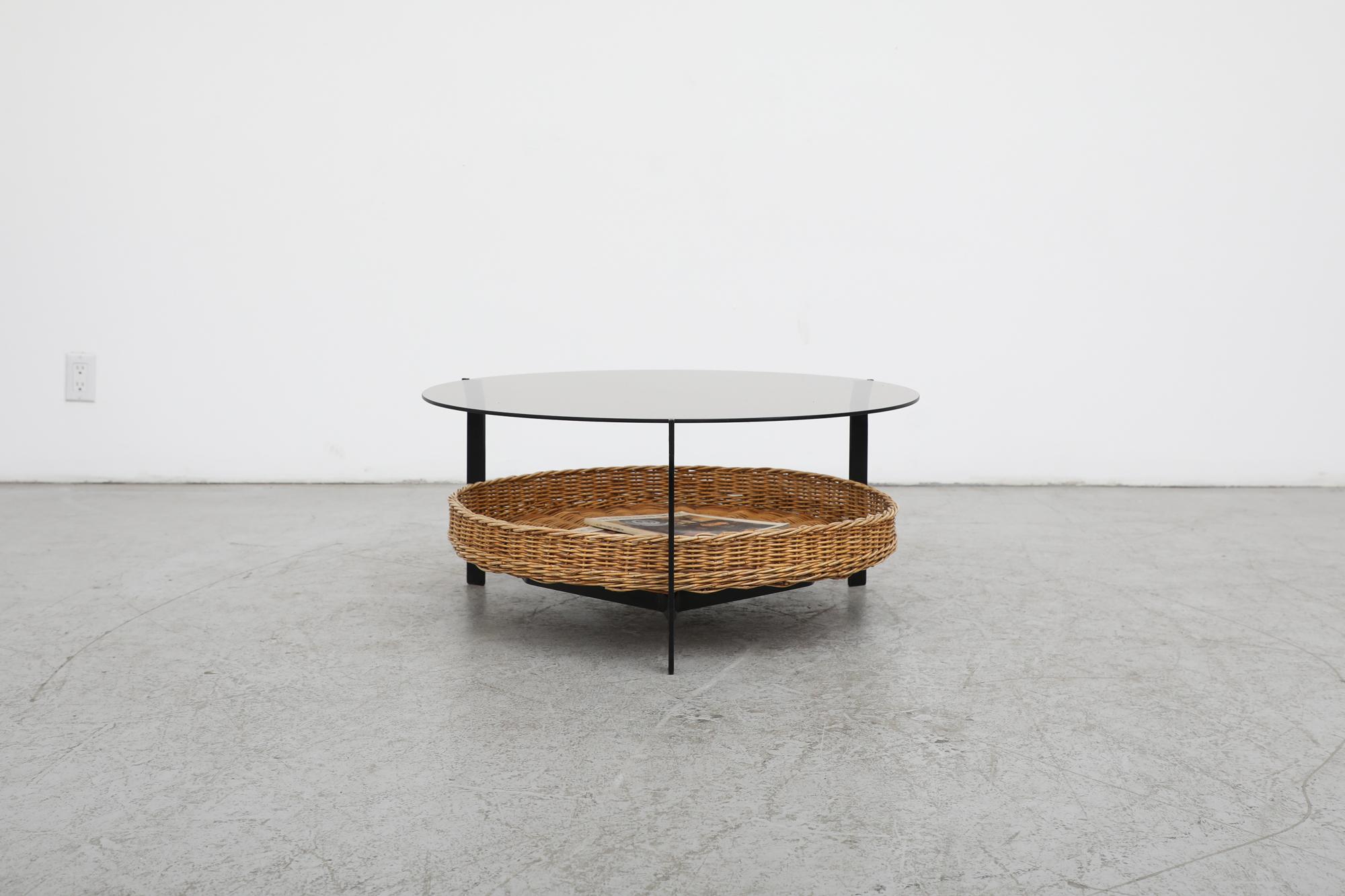 Mid-century, Gebr. Jonkers manufactured, early 1960s, round smoked glass coffee table with lower woven wicker basket on black enameled metal frame. Attributed to designer Dirk van Sliedregt, who was instrumental in translating the use of rattan and