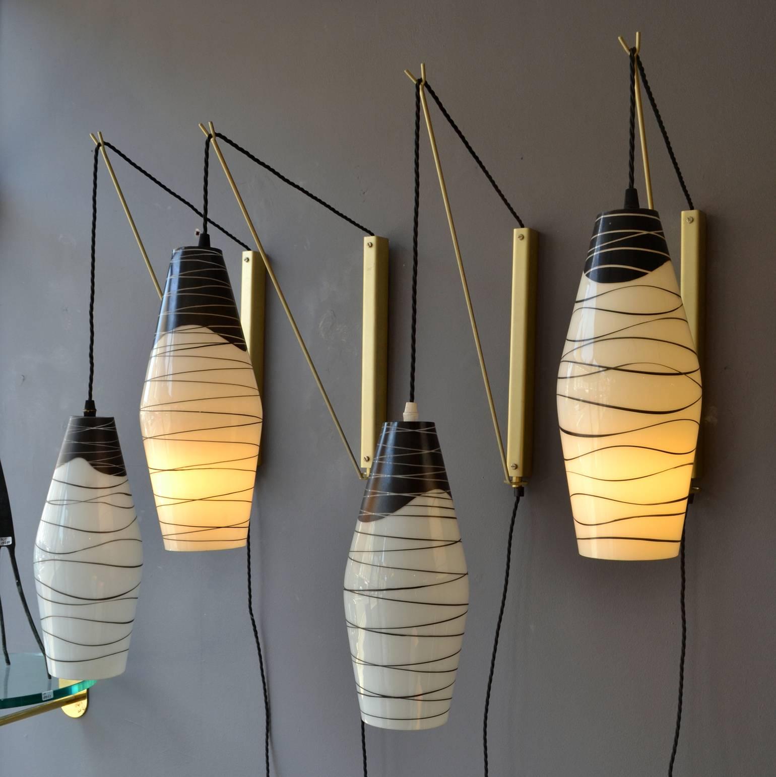 Two pairs of wall-mounted pendants with opaline shades hand-painted in black hanging of black braided flex on an adjustable bronzed metal bracket. The height of the flex can be adjusted and the metal bracket allows the lamps to hang closer or