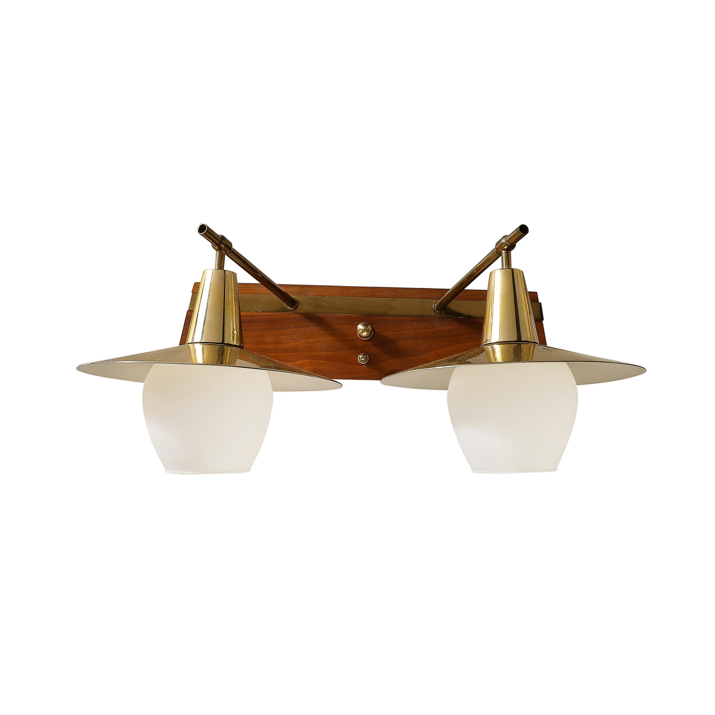 Voici une exceptionnelle applique à deux têtes de style moderniste du milieu du siècle, fabriquée au Danemark vers 1960. Cette pièce sophistiquée allie l'élégance du laiton, le charme subtil du verre dépoli et la chaleur du bois de teck pour créer