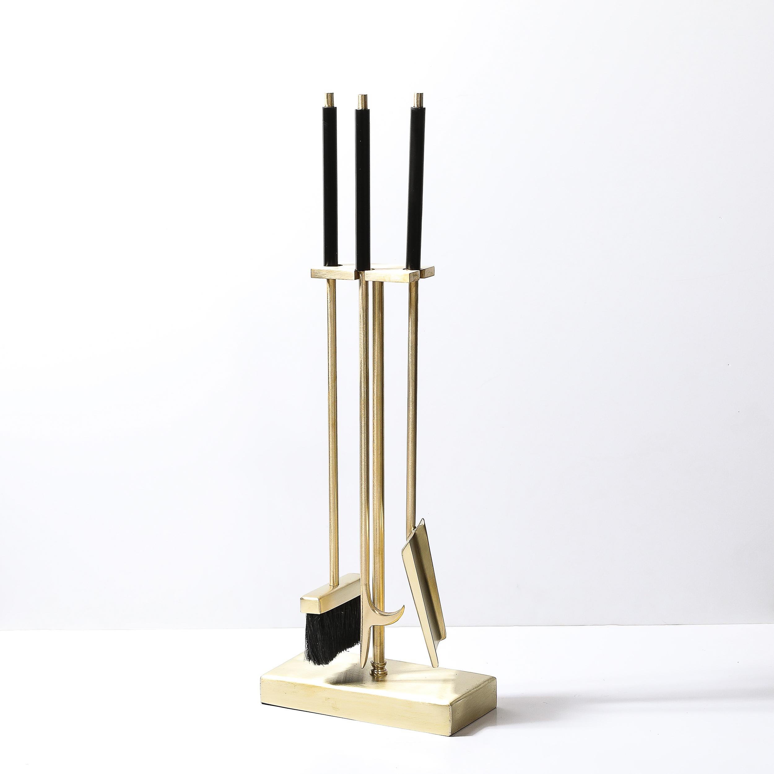 Questo set di attrezzi da fuoco modernista del Medioevo in ottone spazzolato e smalto nero proviene dagli Stati Uniti del XX secolo. Presenta tre utensili appoggiati su un raccordo rettangolare in ottone che poggia su un supporto cilindrico che