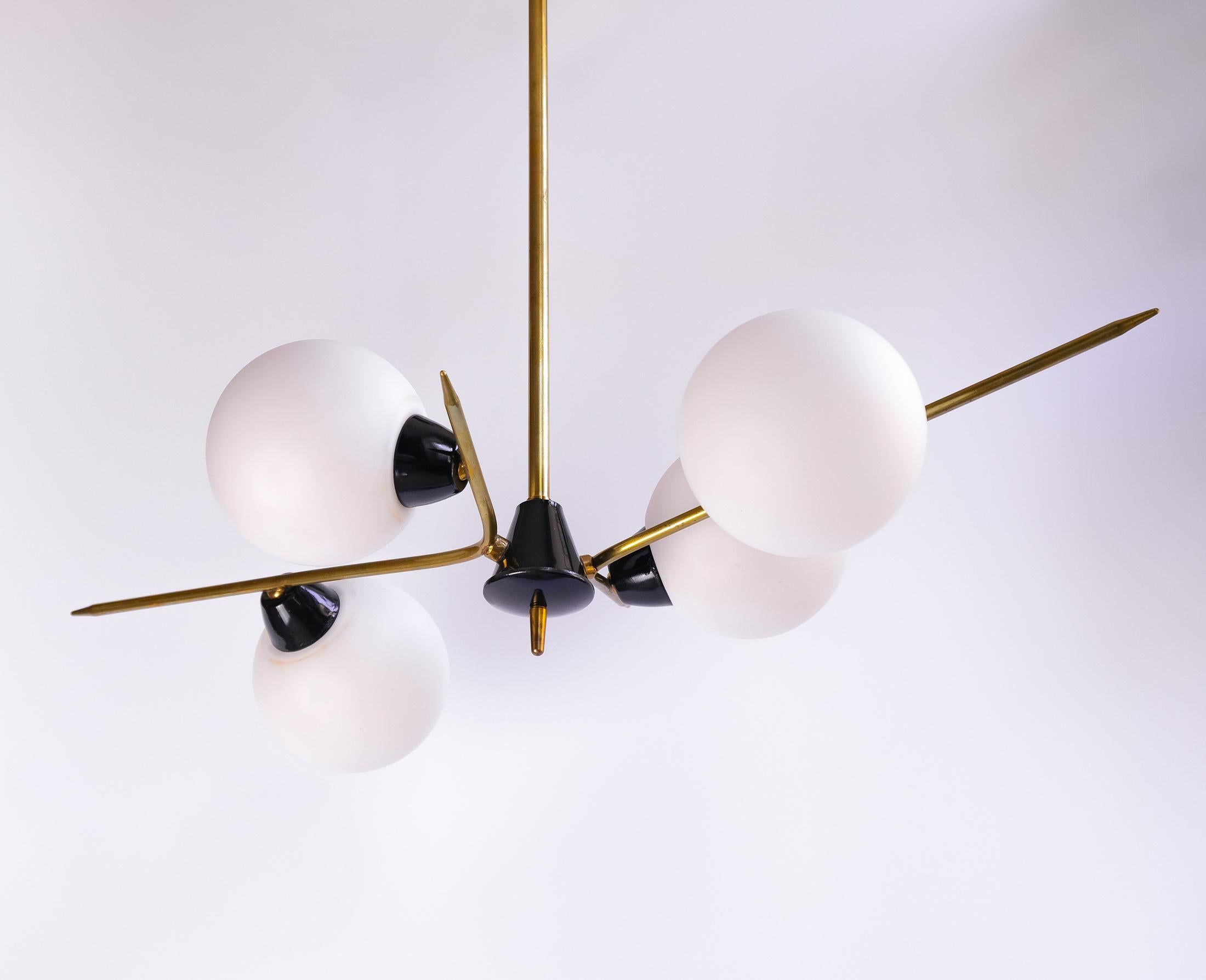 A wonderful Mid-Century Modernist French four-light chandelier, in-the-manner-of Maison Arlus and dating from circa 1950s. The lamp consists of brass and black lacquered metal and has 4 cased-glass opaline globes.

In working order, with its