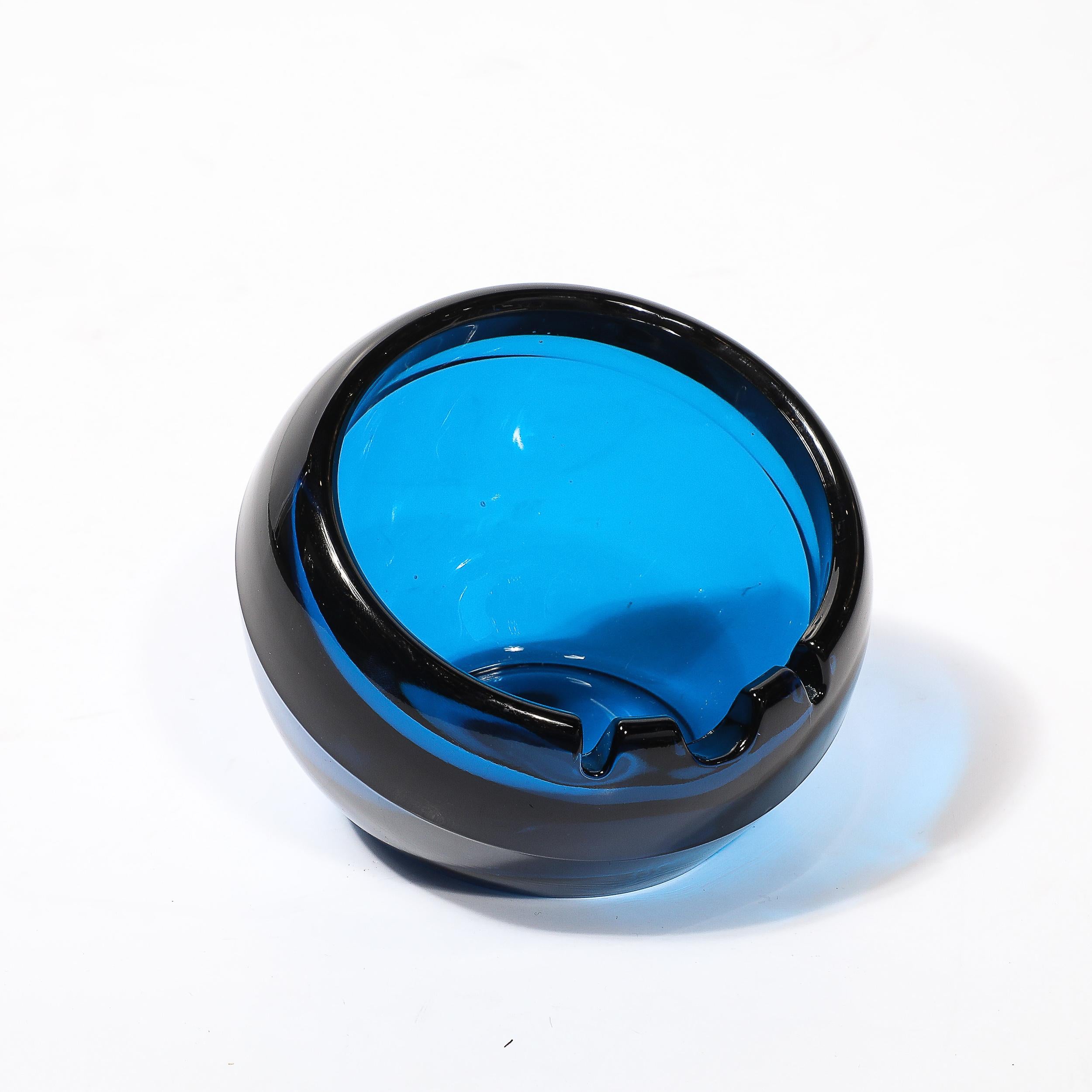Questo elegante vassoio/piatto modernista di metà secolo, soffiato a mano a Murano, Italia, intorno al 1960, incarna la raffinatezza senza tempo e l'eccezionale maestria del vetro di Murano. Realizzato in un profondo e ricco blu cobalto, la forma