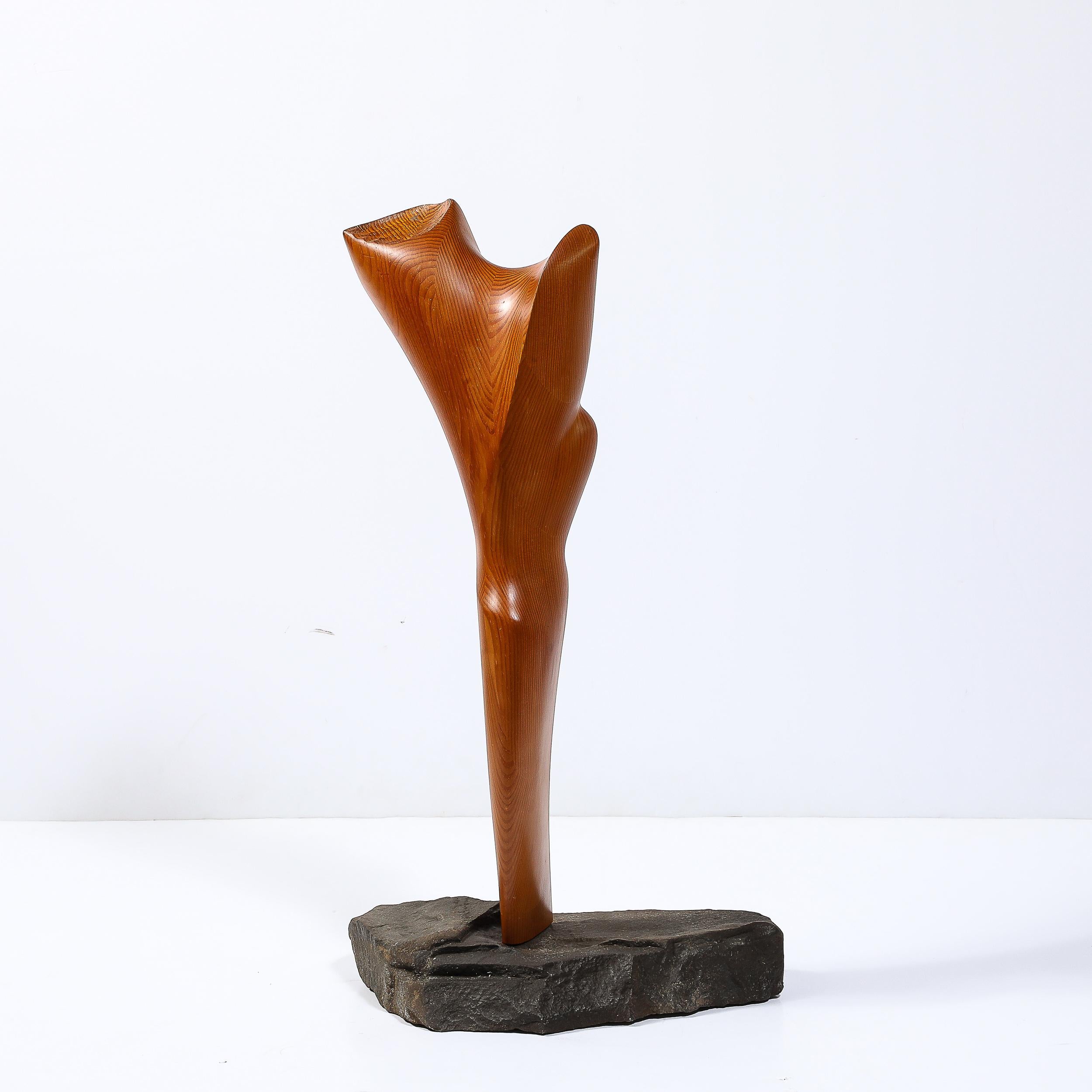 The sculpture rests on a natural stone base, which has been left with a raw finish that contrasts beautifully with the polished, intricate surfaces of the wood. This excellent contrast of materials is highly characteristic of Mid-Century Modernist