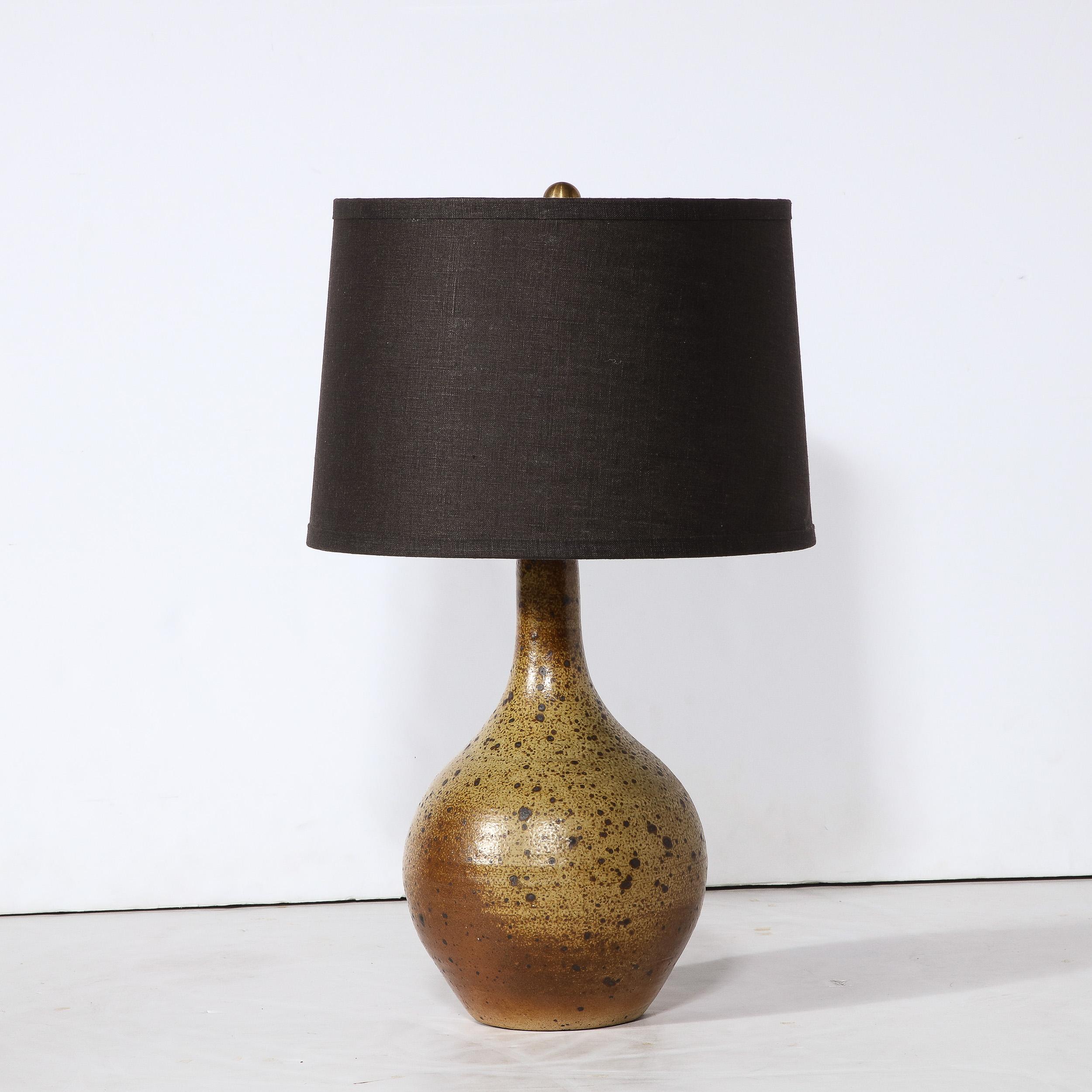 This sophisticated Mid-Century Modern table lamp was realized in France circa 1960. It features a tear drop form with a protuberant base that tapers to a conical neck in a rich palate of earth tones. Hand glazed with a speckled lava like texture