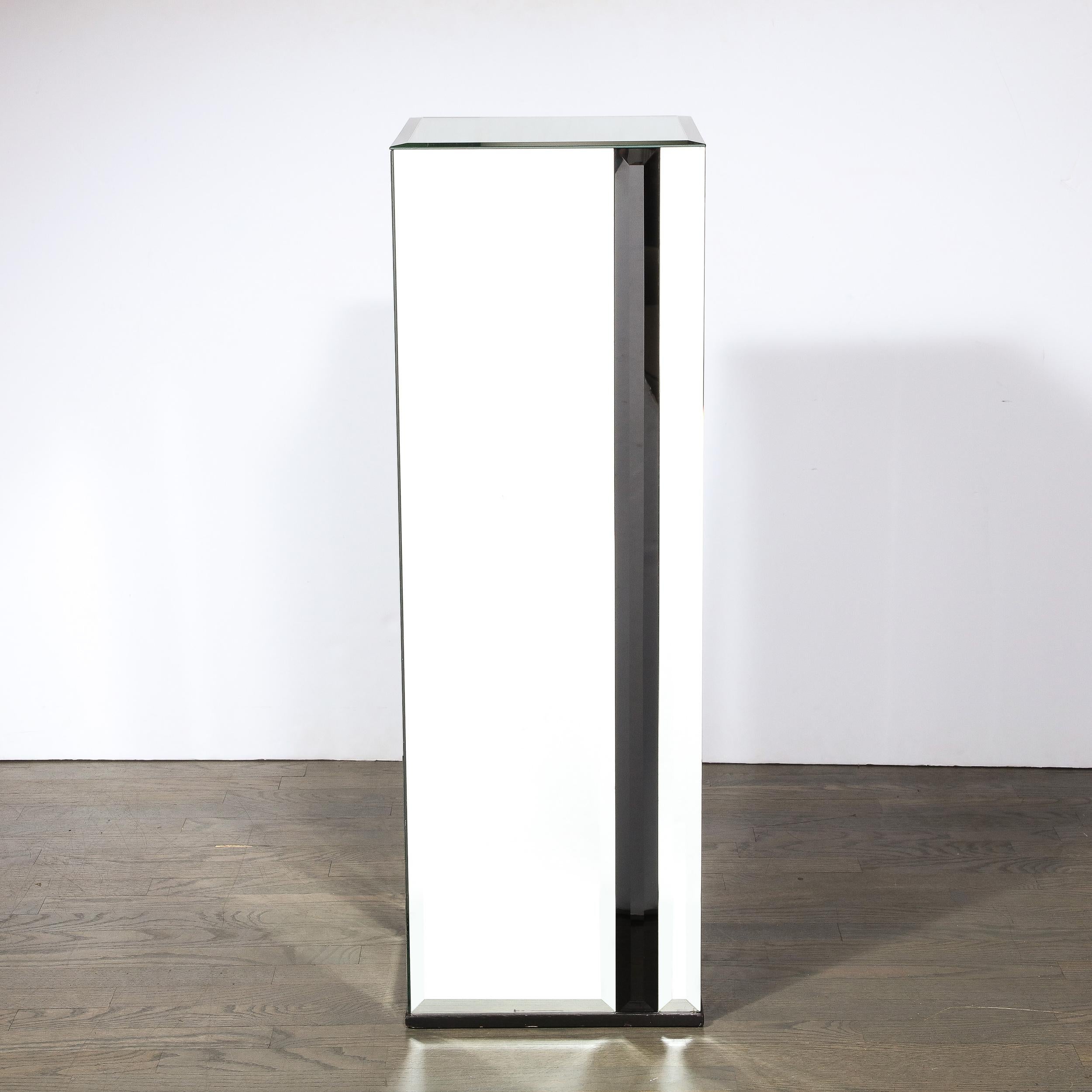 This stunning and sophisticated Mid-Century Modern pedestal was realized in the United States circa 1970. It offers a rectangular volumetric body composed of mirrored glass segments. Each side offers a larger rectangular mirrored panel with a thin