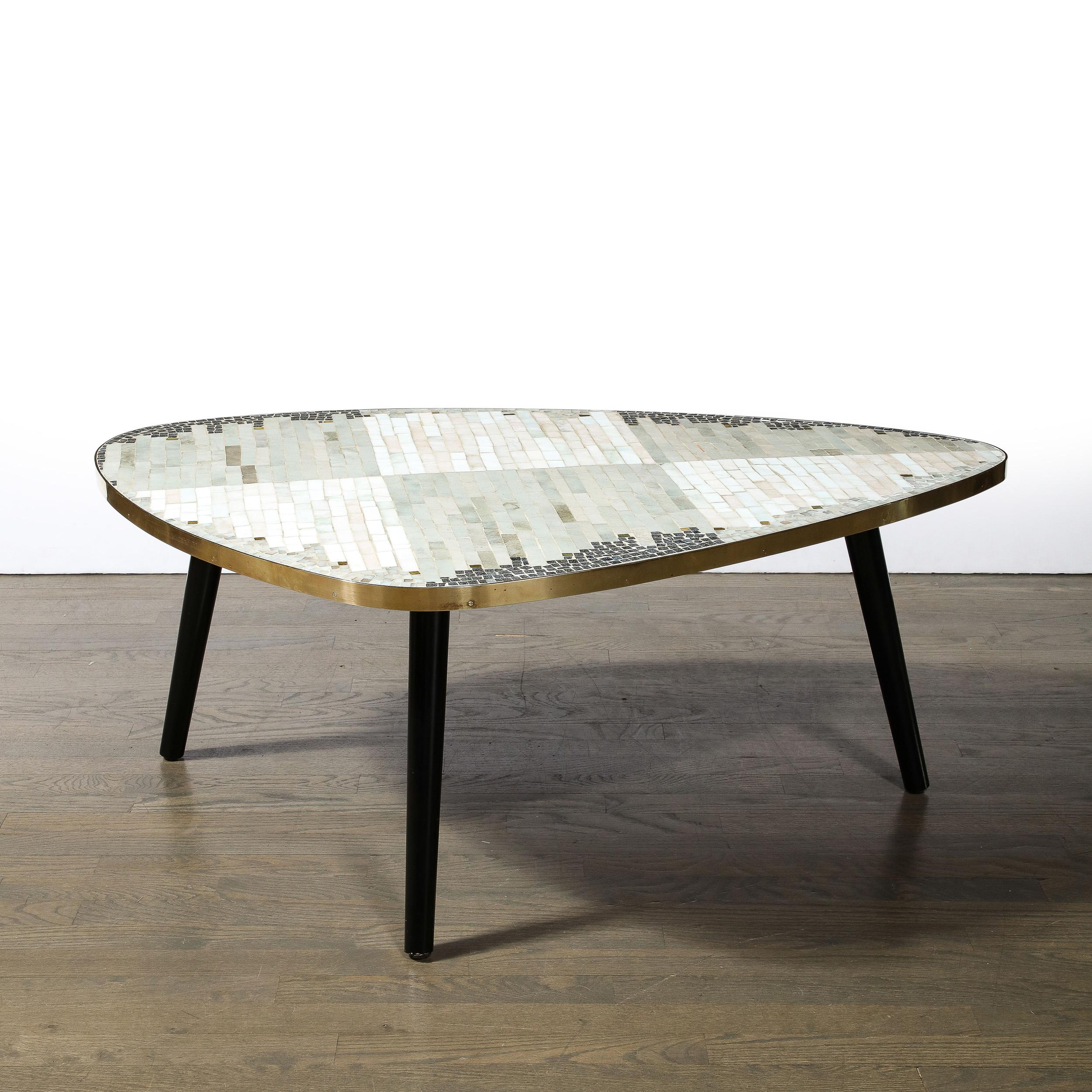 This beautiful Mid-Century Modern cocktail table was realized in France circa 1960. It features a vaguely triangular amorphic form with rounded corners. The perimeter of the piece is wrapped in brass while the interior of the top offers a fantastic
