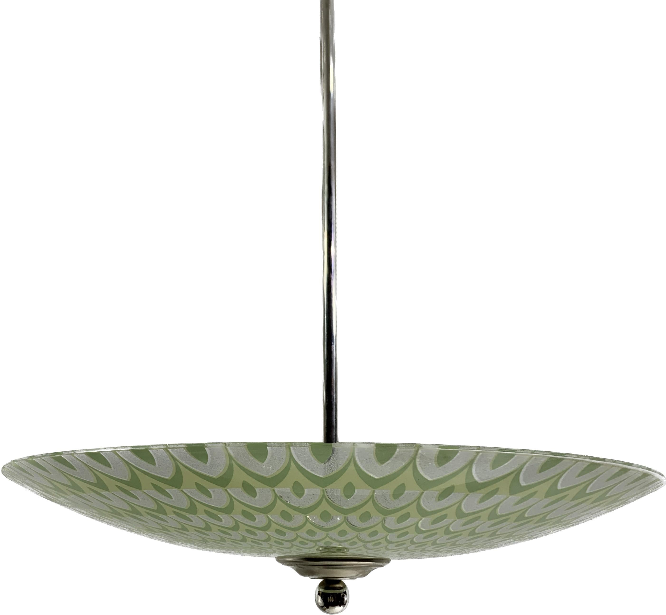 French art Deco modernist pendant light. The structure is metallic. The glassware is in tones and hues of green and lighter green, representing geometric circular patterns spiralling all around the lampshade. These designs and colours are typical of