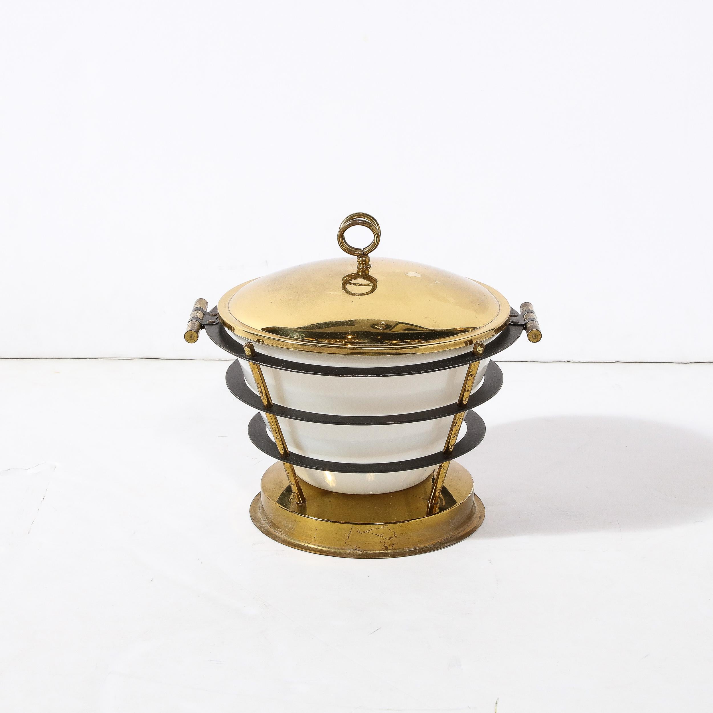 This elegant and sculptural ice bucket was realized in Italy, circa 1960. It offers a circular faceted polished brass base with three cylindrical supports tracing the exterior of the conical white glass center. The brass supports pierce through