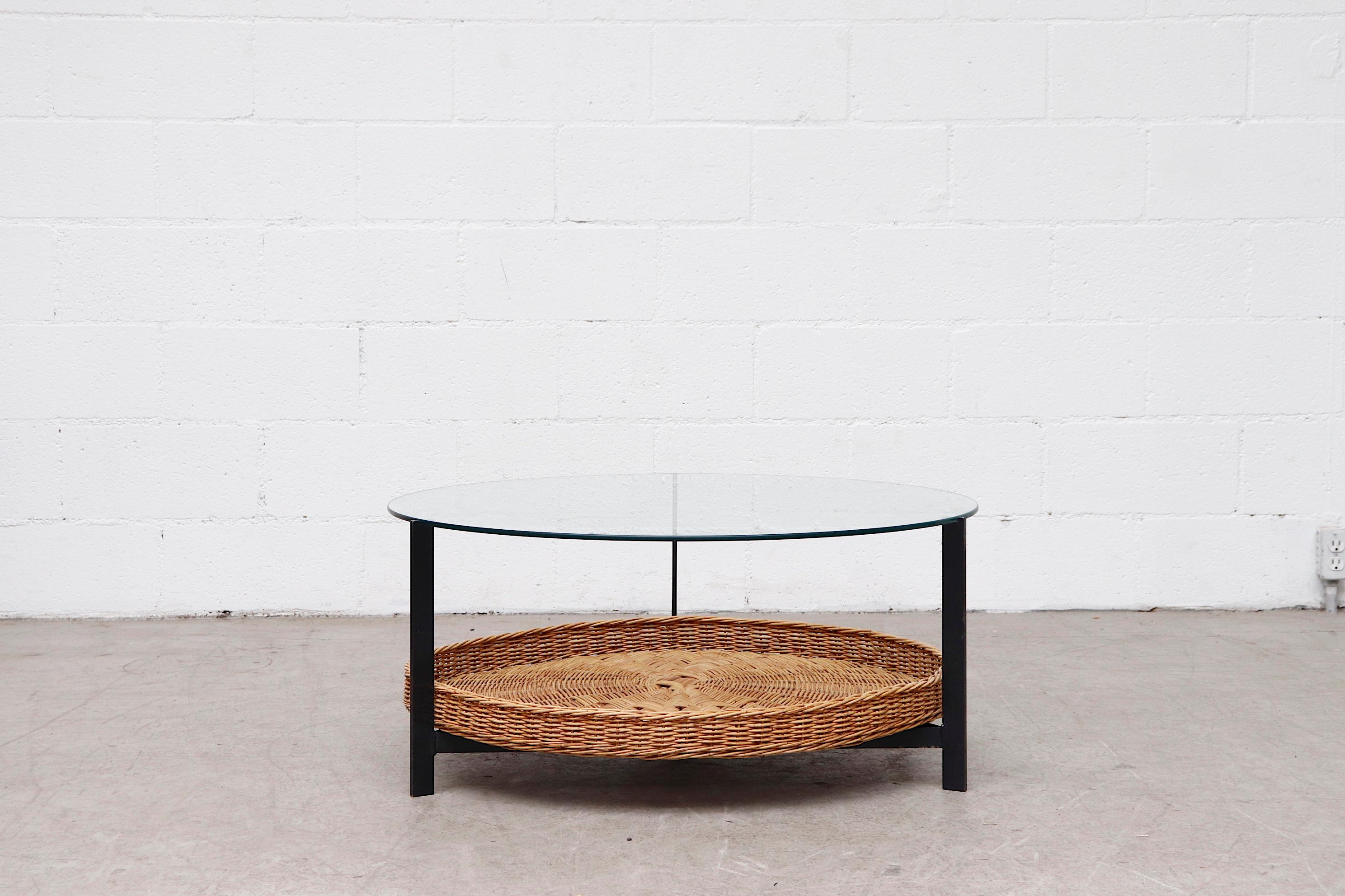 Midcentury round glass coffee table with lower woven wicker basket on charcoal grey enameled metal frame and round plate glass. In original condition with heavy patina to the frame and glass. Visible wear and scratching consistent with its age and