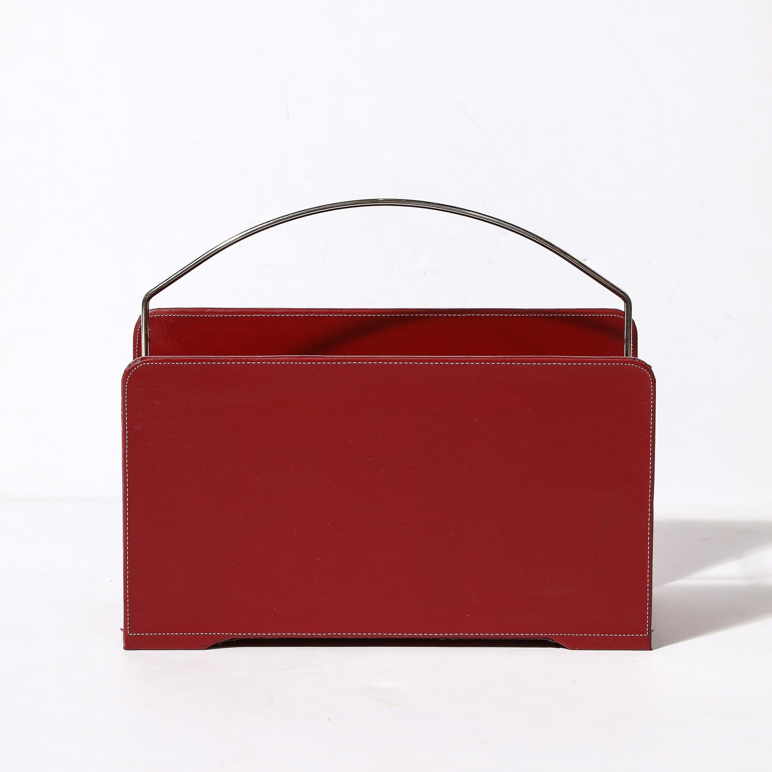 This sleek and well crafted Mid-Century Modernist Red Leather and Chrome Magazine Holder is in the manner of Adnet and originates from the United States, Circa 1960. Featuring a chrome cylindrical frame and handle supporting hand-stitched panels in