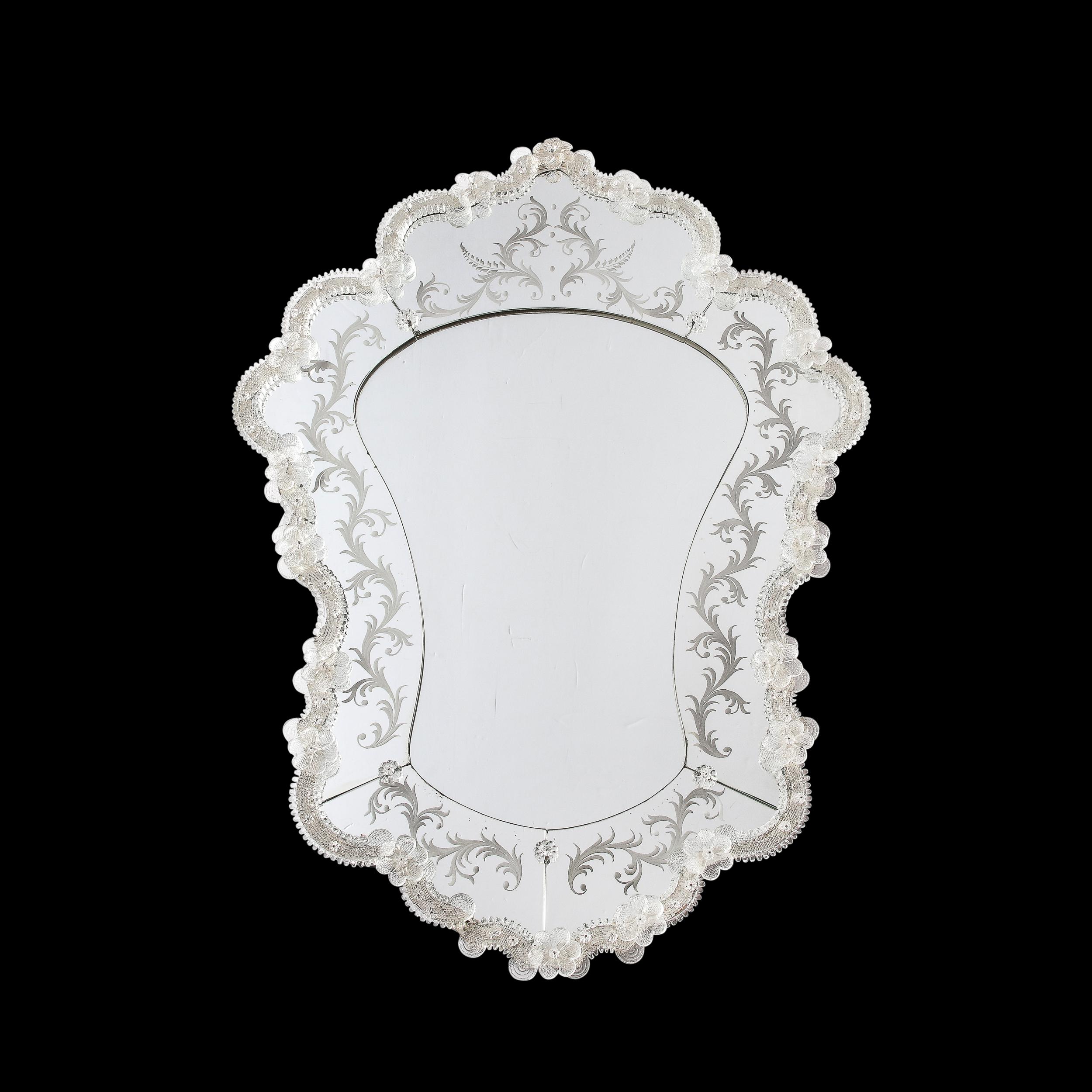 This highly adorned and well crafted Mid-Century Modernist Venetian Mirror with Reverse Etched Detailing and Murano Appliqués originates from Italy, Circa 1960. Features a scalloped shield form profile, the piece is lined with hand-blown and