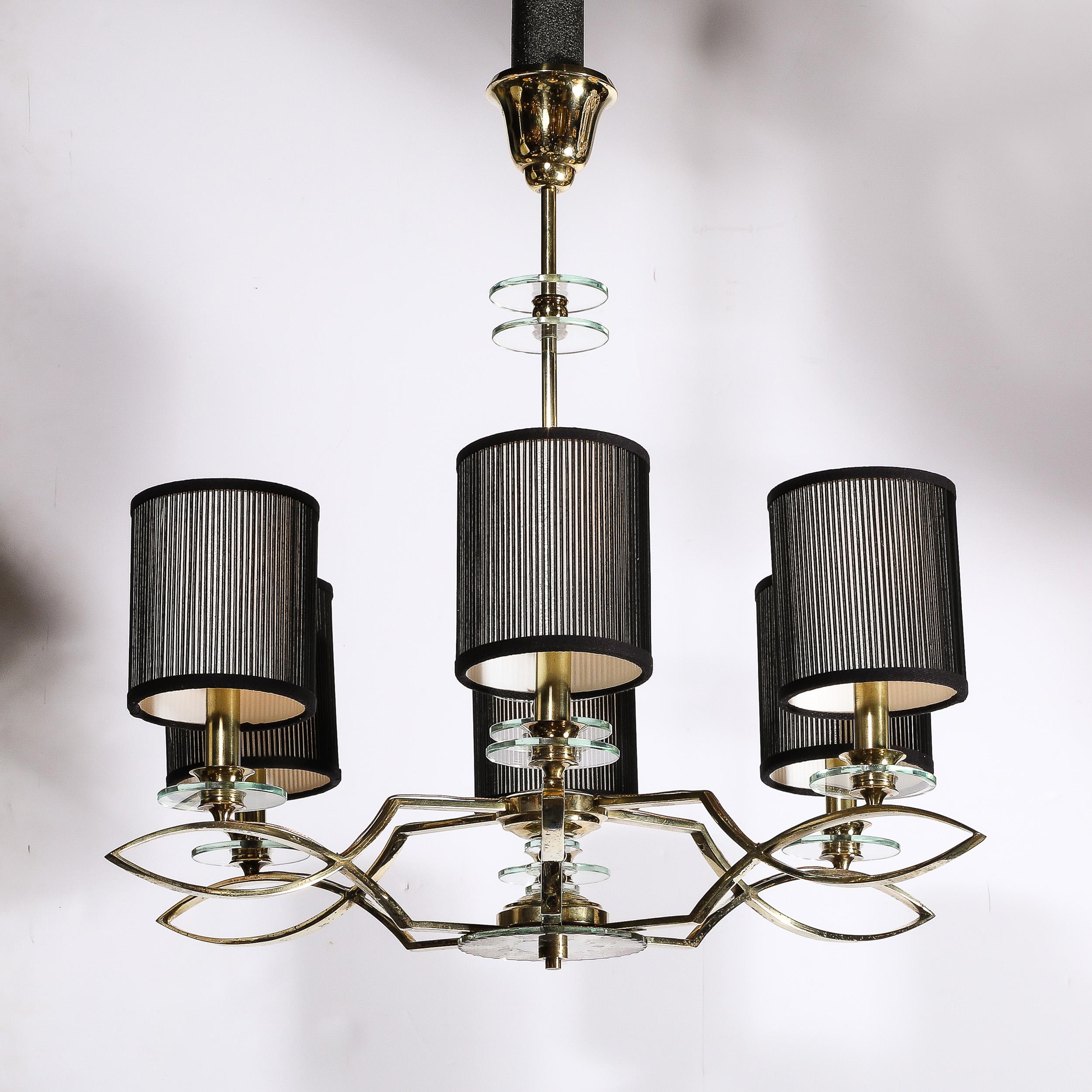 This glamorous yet reserved Mid-Century Modernist Six Arm Chandelier in Brass, Glass, and Antiqued Mirror originates from France, Circa 1950. Featuring a brass laticework frame of intersecting curves and right angles, round transparent glass disks
