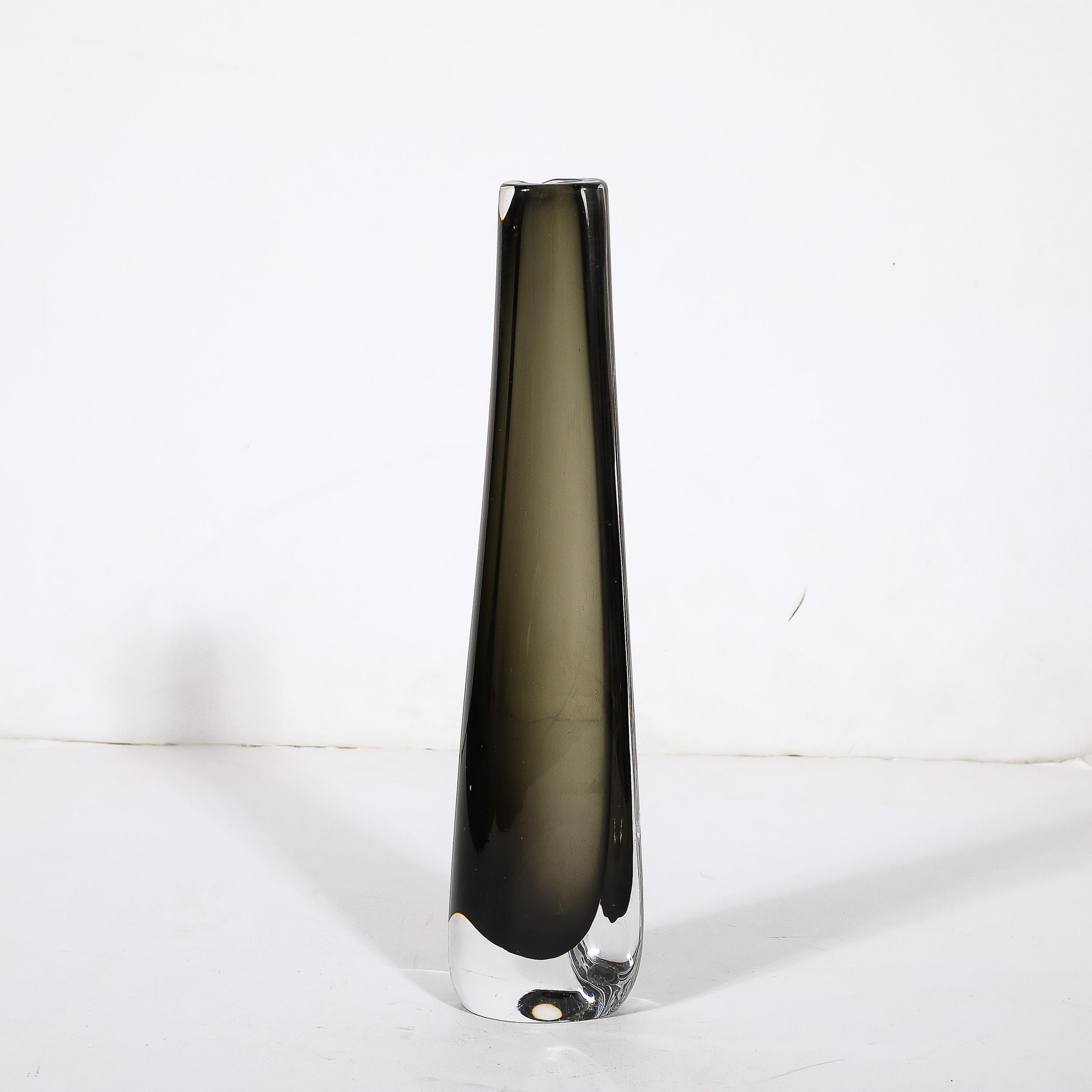 This sleek and reserved Mid-Century Modernist Slender Smoked Glass Vase is by Nils Landberg for the esteemed art glass company Orrefors, and originates from Sweden, Circa 1960. Features a flattened base with transparent glass on the outside surface