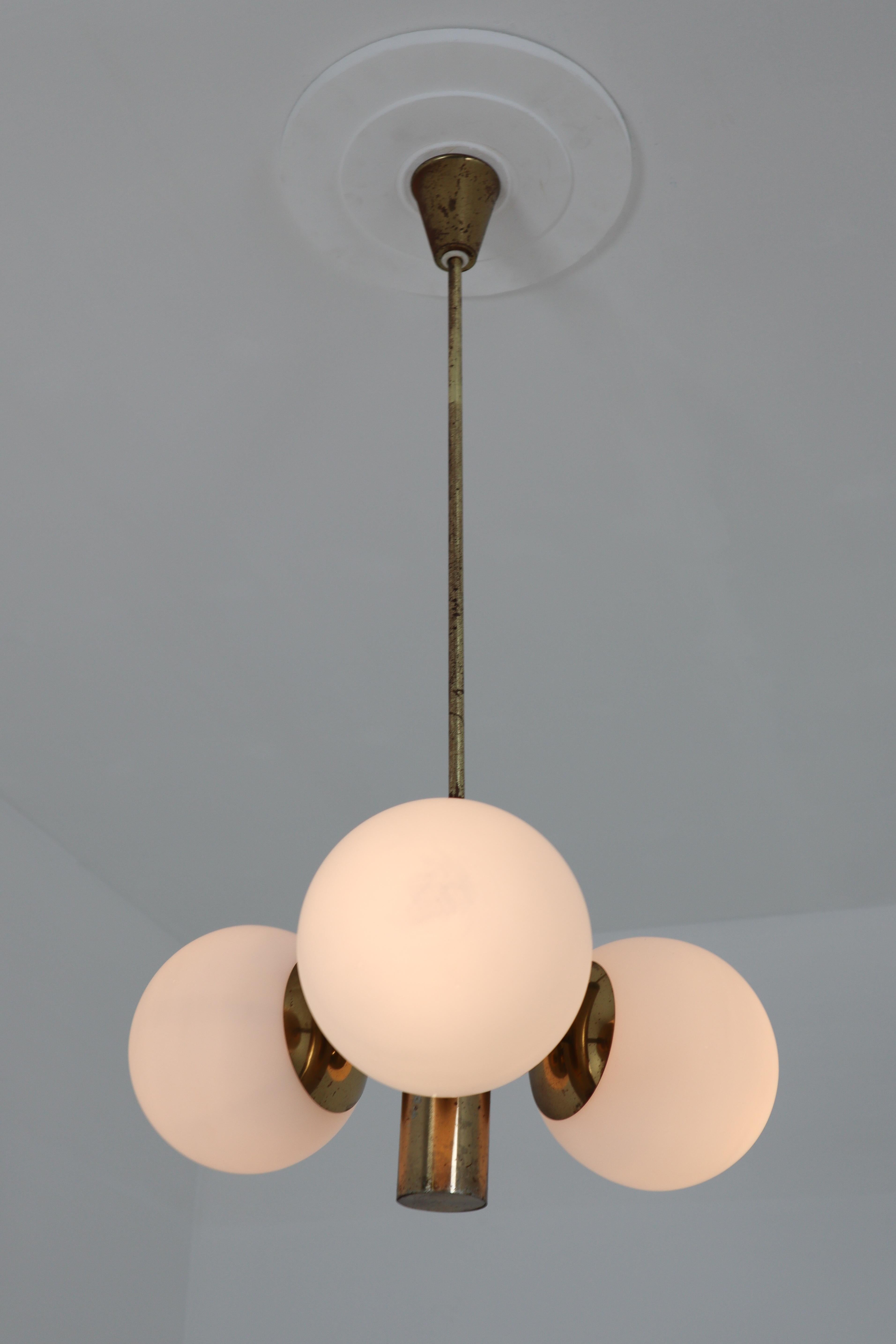 This fantastic Mid-Century Modernist sputnik chandelier was designed in Germany 1960s featuring a patinated brass frame and three handblown opal glass globes.

     