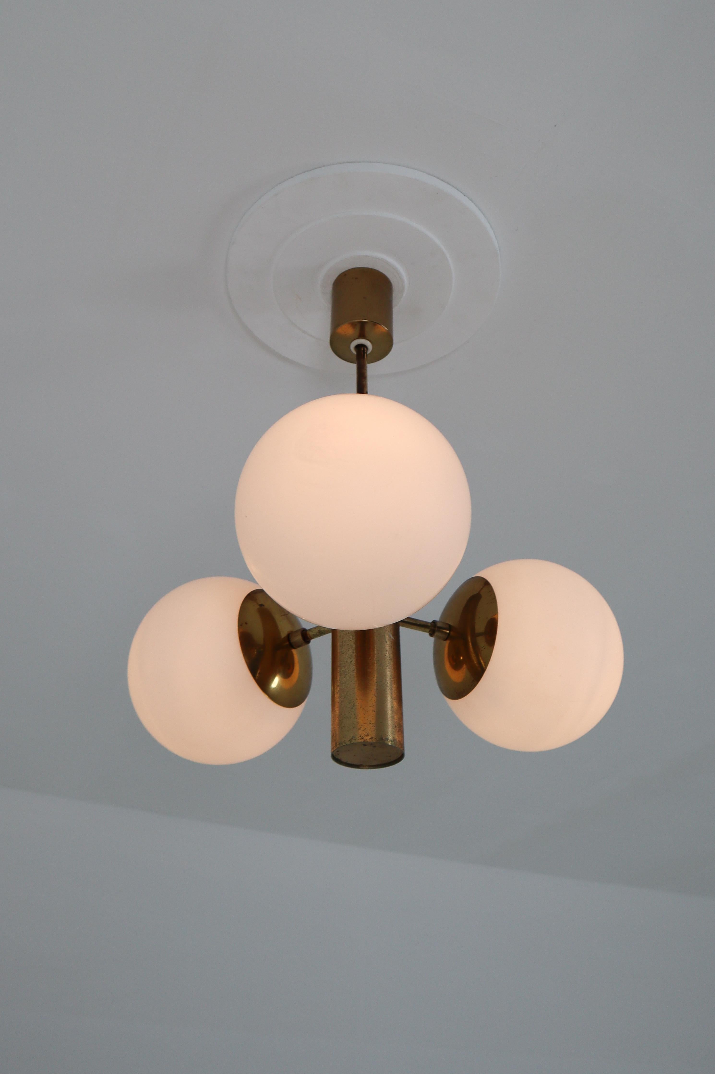 Mid-Century Modernist Sputnik chandelier was designed in Germany 1960s featuring a patinated brass frame and three handblown opal glass globes.