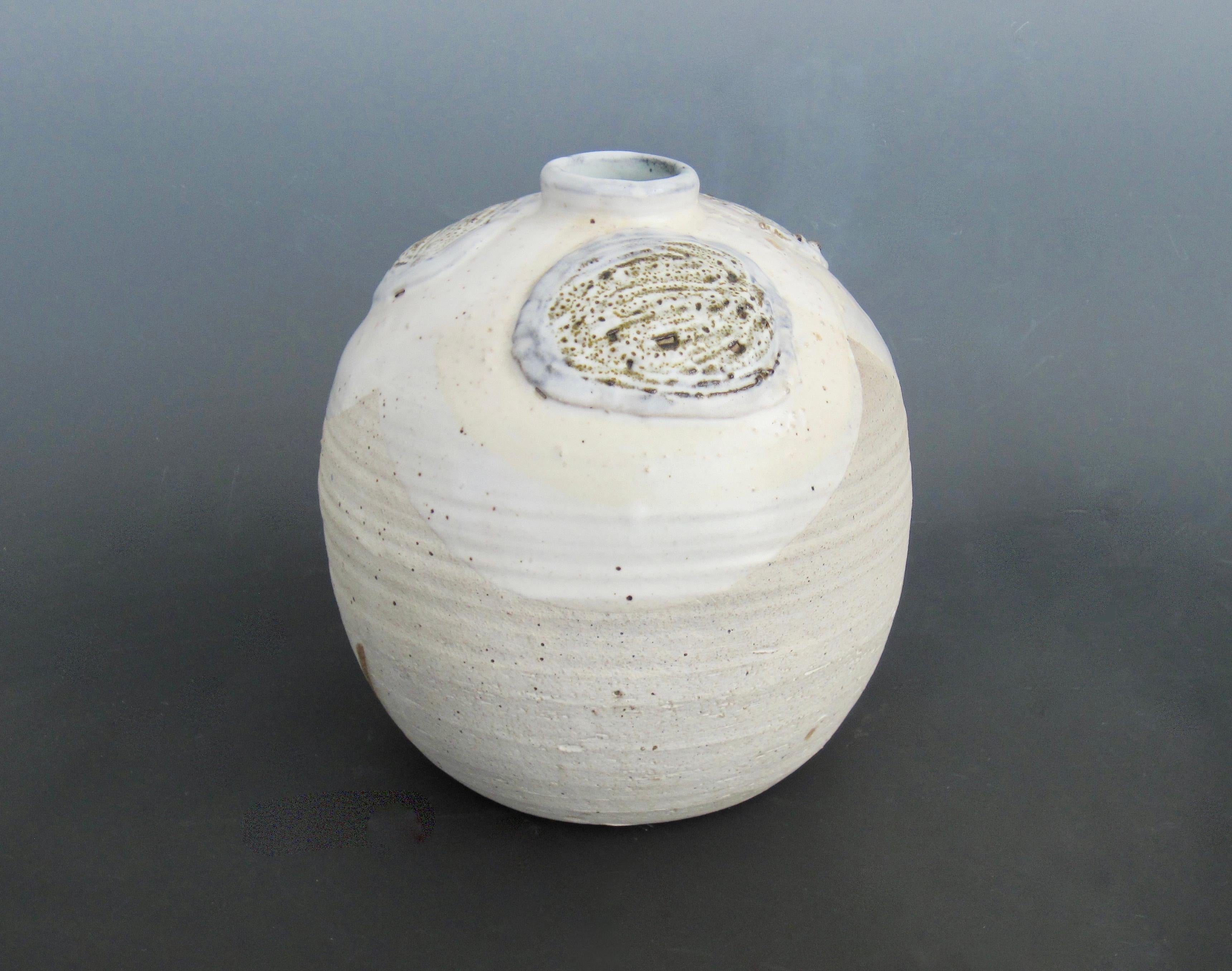 Mid-century modernist signed stoneware pottery vase in shades of white and tan. Three glazed textural circular motifs around the bottleneck and repeating circumference lines to the bottom make this vase visually and proportionally pleasing to the
