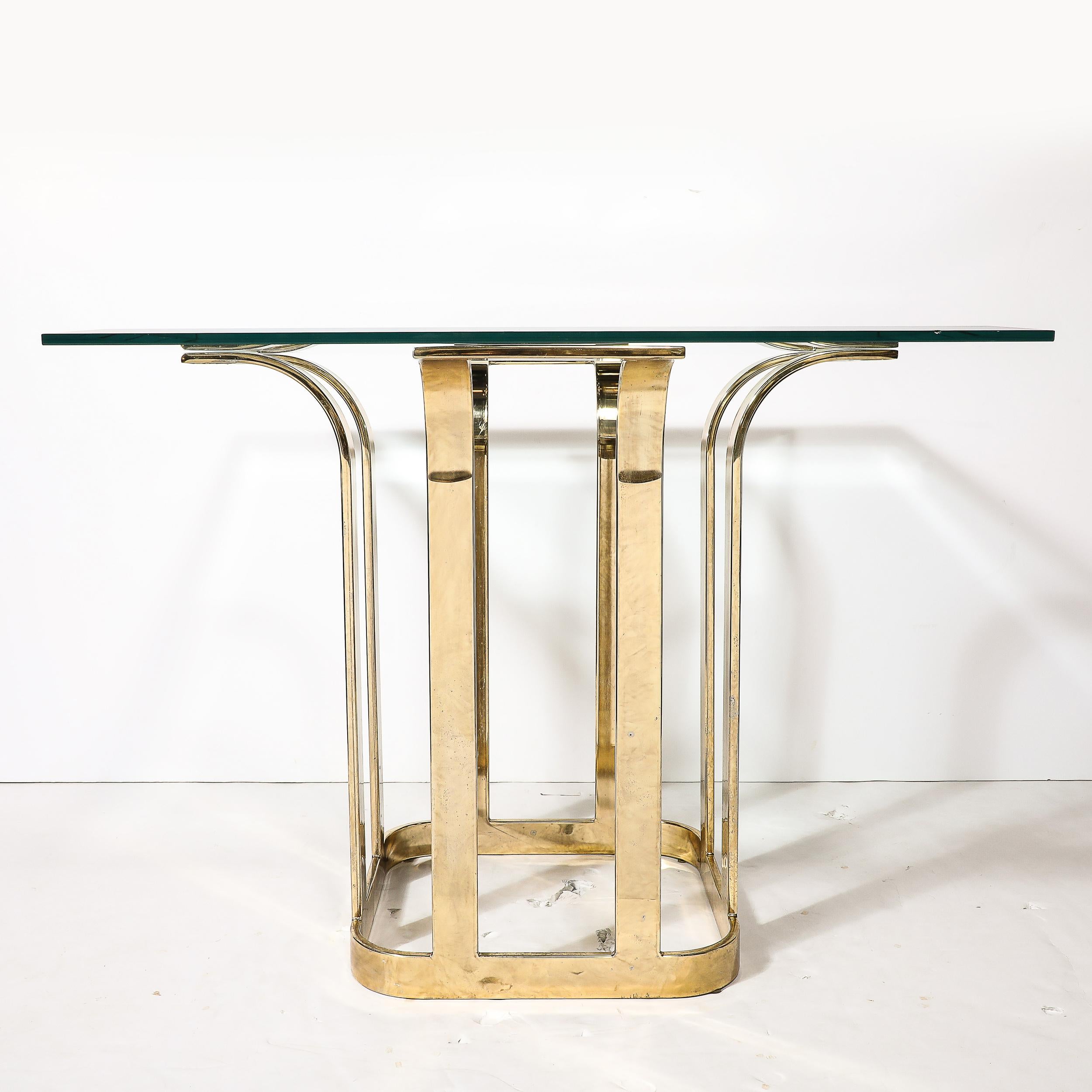 Cette magnifique table de salle à manger avec plateau en verre, de style moderniste du milieu du siècle, en forme de tulipe stylisée en laiton, provient des États-Unis, vers 1975. La base est carrée avec des coins arrondis, et quatre éléments