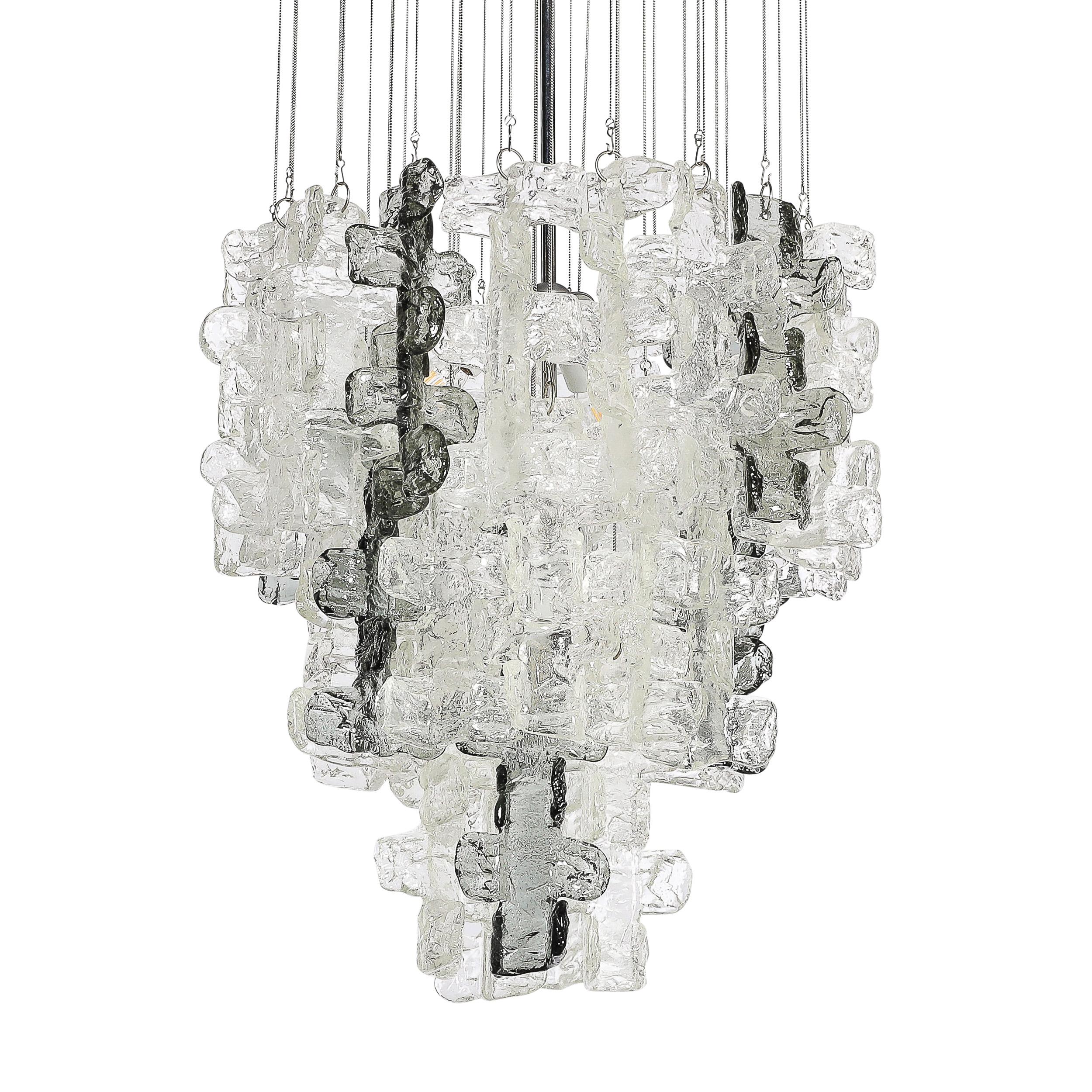This captivating Mid-Century Modernist Textural Clear and Smoked Glass Chandelier with Chrome Fittings is by the esteemed glass artist Mazzega and originates from Italy, Circa 1970. Features a nested composition of hanging hand-blown glass elements