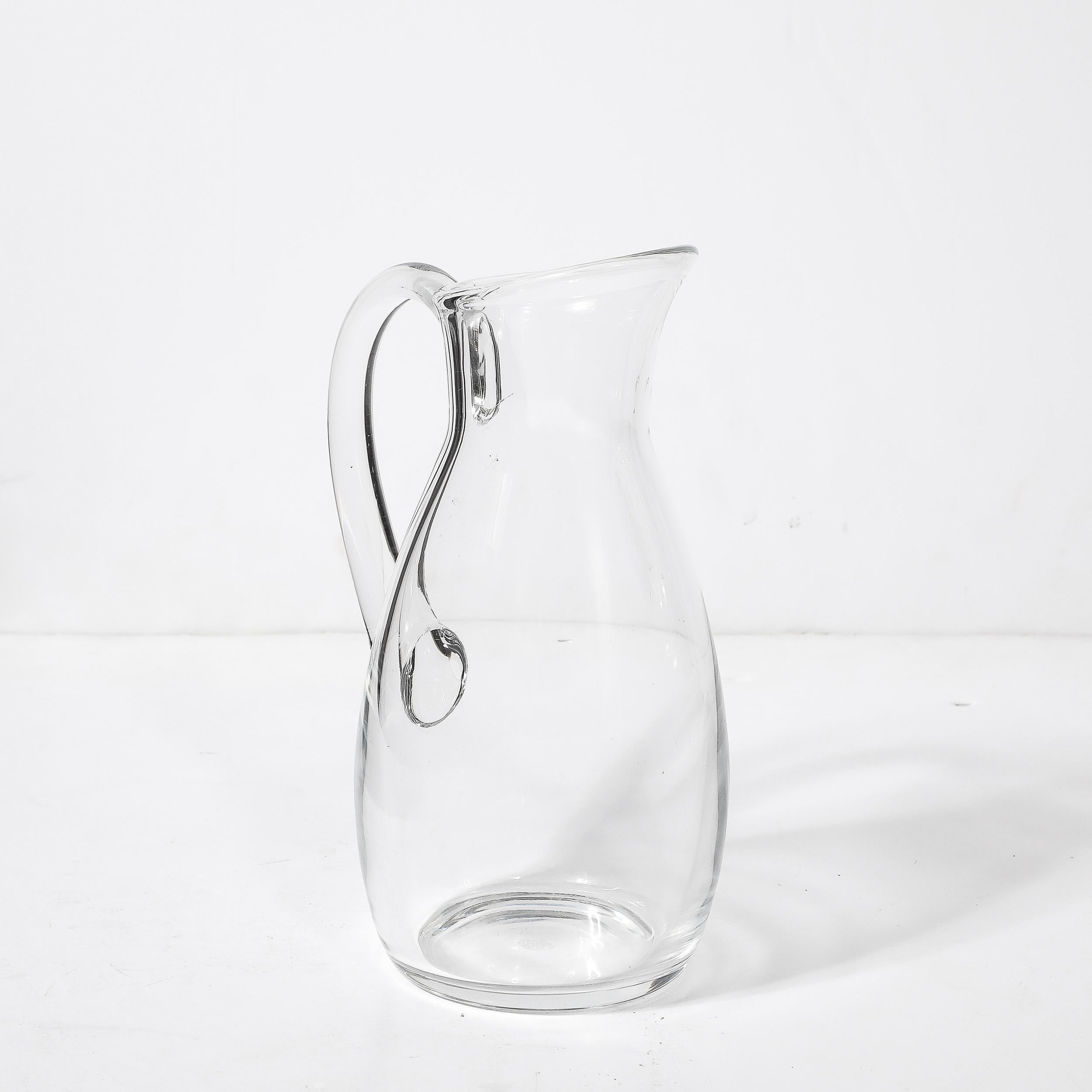 This Mid-Century Modernist transparent crystal pitcher is a stunning example of elegance and functionality, created by the renowned French glassmaker Baccarat around 1960. The pitcher's clean lines and minimalist design capture the essence of