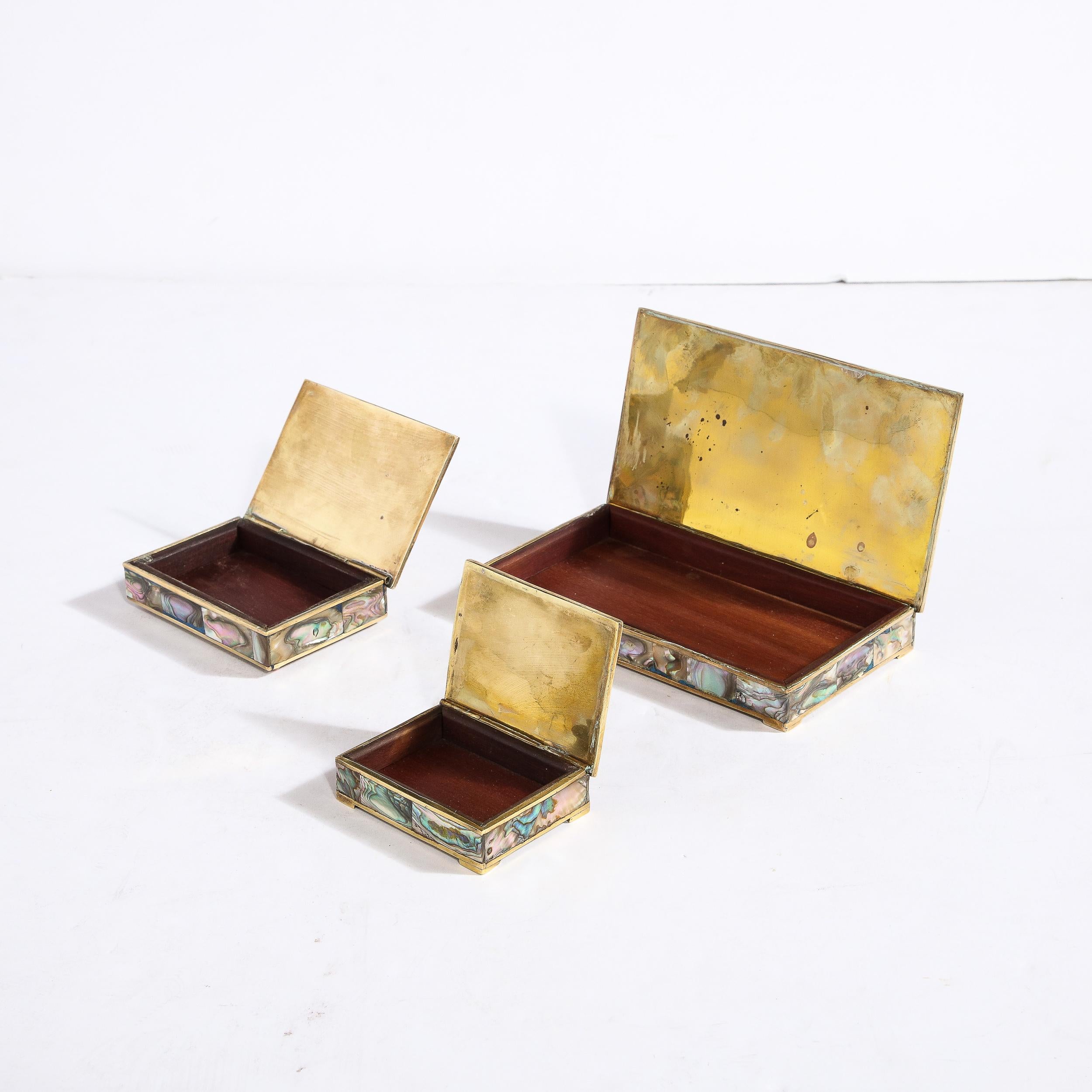 This striking set of Mid-Century Modern trinket boxes were realized in the Philippines circa 1960. They feature abalone clad exteriors showing the inherent beauty of the shell- with its organic texture and iridescent skein with an abundance of muted