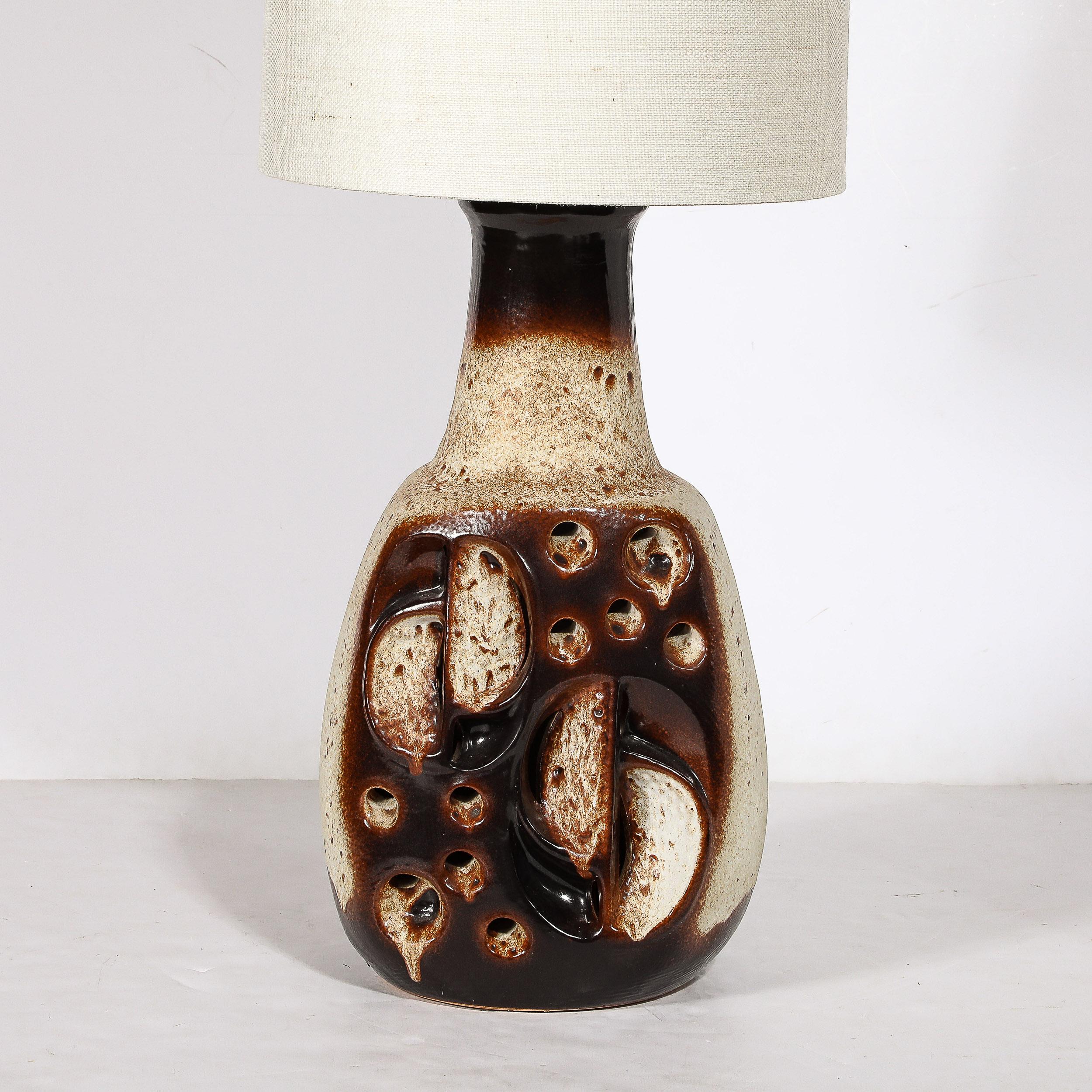 Cette lampe de table en céramique volcanique émaillée avec ouvertures éclairées, bien dimensionnée et matériellement dynamique, est une œuvre de Hustadt Leuchten, originaire de France, datant de 1970. Naturellement, le corps sculptural arrondi en