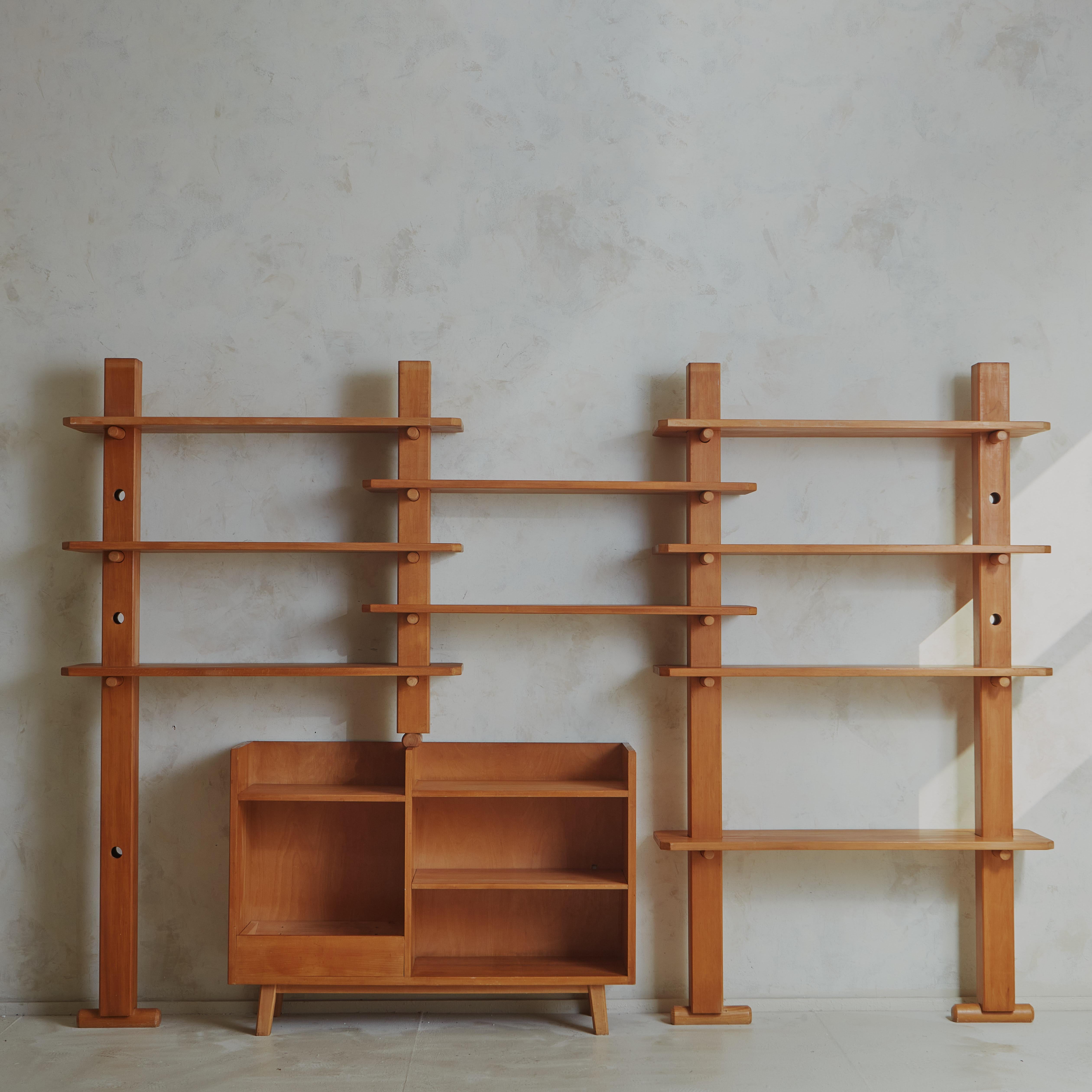 A stunning Mid Century etagere constructed with varnished sycamore wood. This modular unit features three shelving modules and a central built-in console. The shelves are supported by circular pegs, which allow them to be rearranged at various