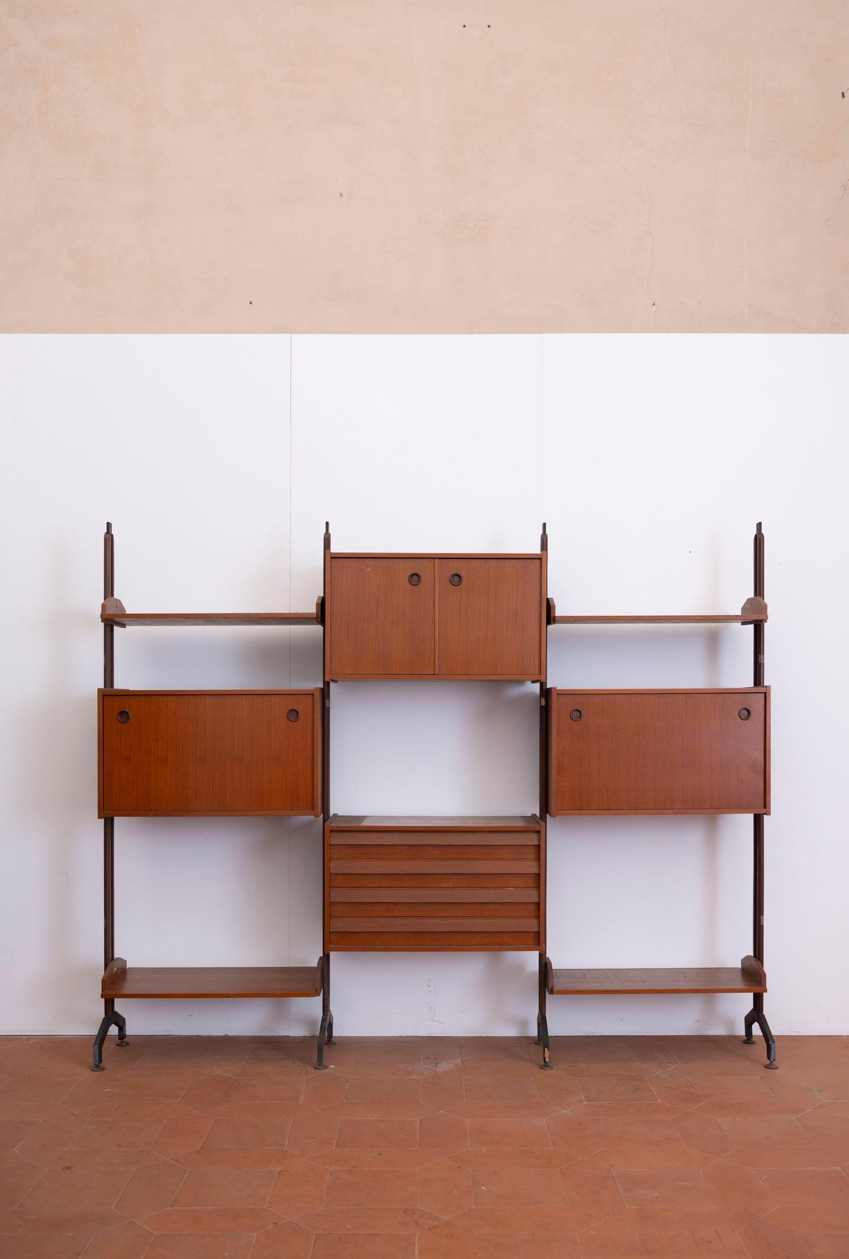 Modular Mid-Century bookcase with wooden structure and gilded brass details. This elegant piece offers versatile storage with four shelves, a central cabinet, four drawers, and two flap-opening compartments on either side.

Italy, 1960s