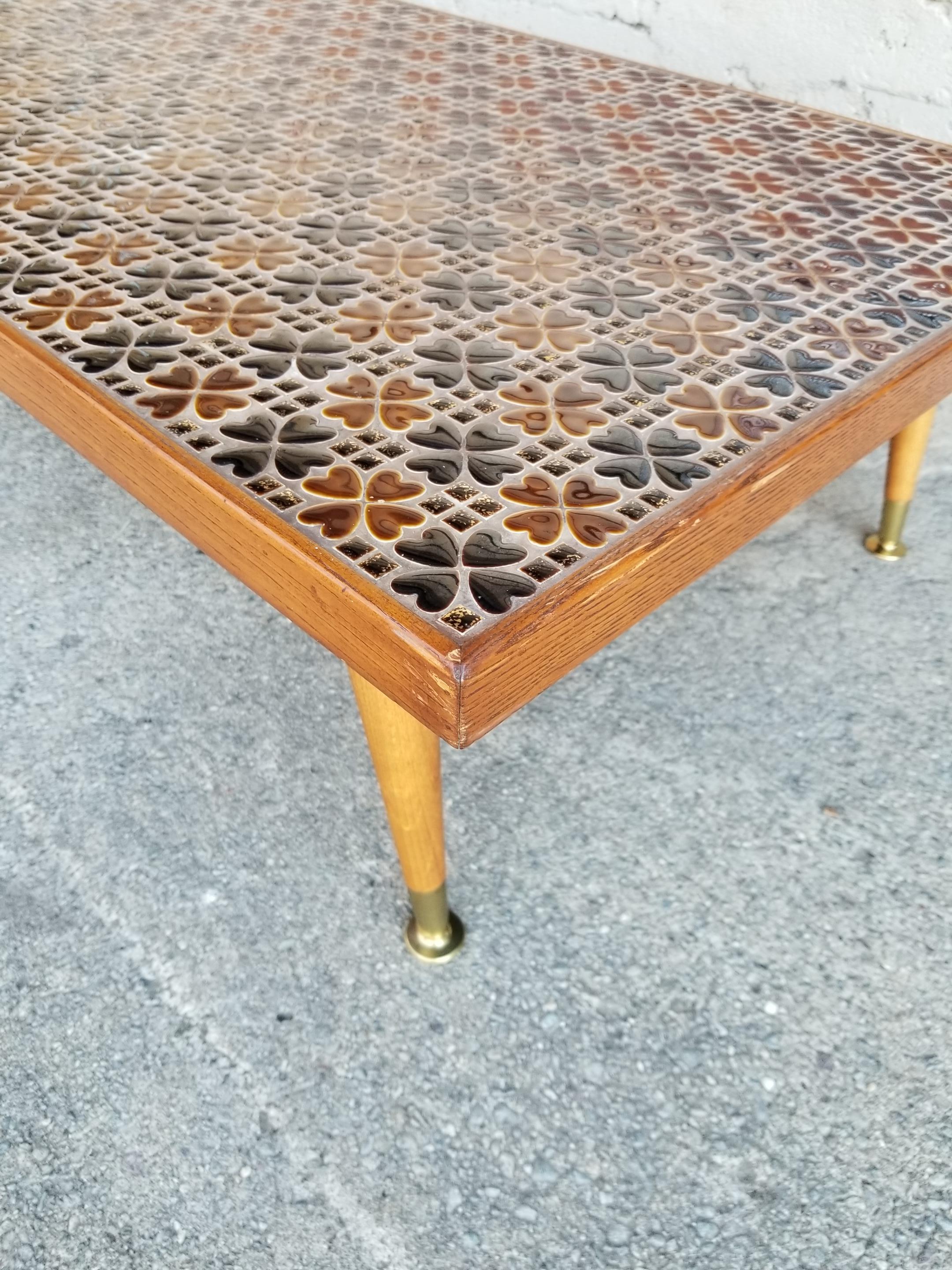 A 1960s mosaic tile top coffee table with Classic peg legs construction. Quality workmanship with expertly patterned multiple form tiles. Notice gold glitter to smallest square tiles. Warm, earth-tone organic colors. Framed in solid oak.