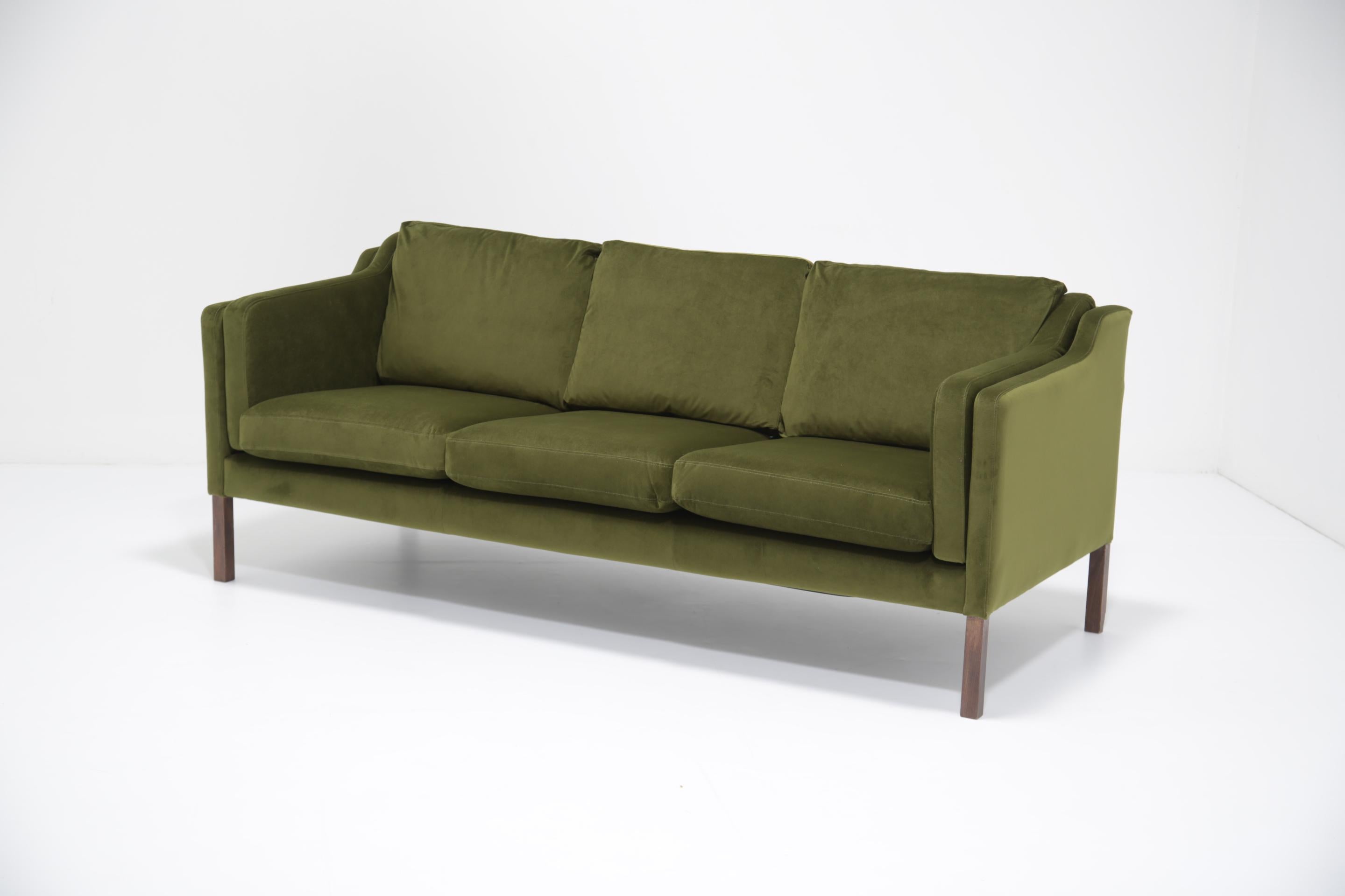 Dai un'occhiata a questo splendido e comodo divano a tre posti, rivestito in velluto verde muschio e dotato di gambe in legno. Questo divano è stato disegnato da Borg Mogensen nel 1962, originariamente per la sua casa personale, ma il progetto è