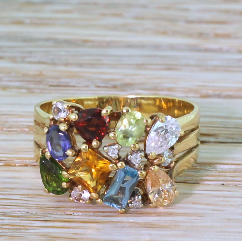 A fun, idiosyncratic multi-gemstone ring, featuring an eclectic mix of stones, cut and colour in a dazzling, a symmetrical design. The cluster sit nice and low to the finger on a wide, double-vented yellow gold shank.

Accompanied by an independent