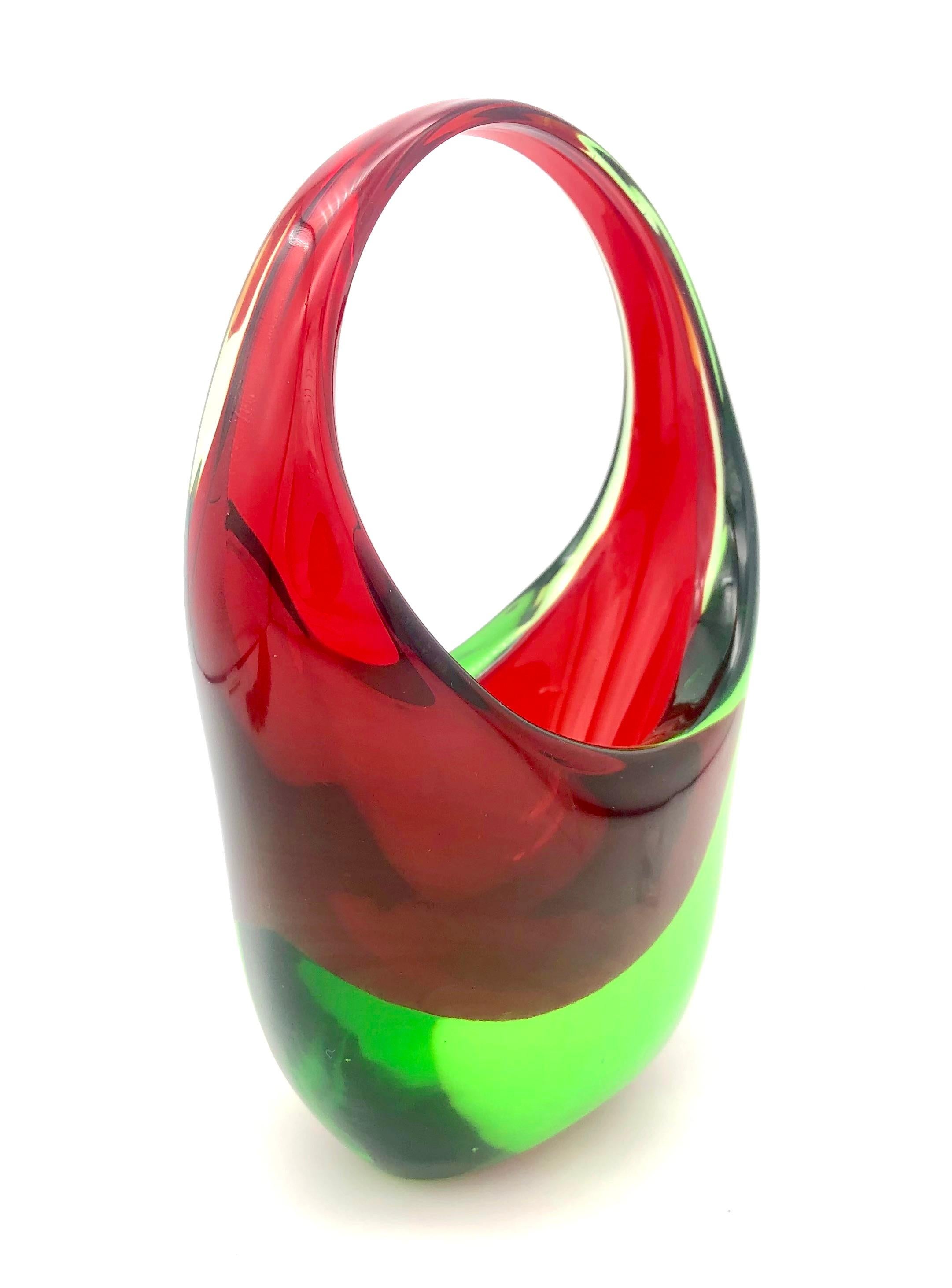This fine chunky piece of Murano glass has been designed as vessel with handle in 1960 ca. The colours used, a  strong red and a strong green, are complementary colours, they stand opposite each other in the colour wheel. Complementary colours have