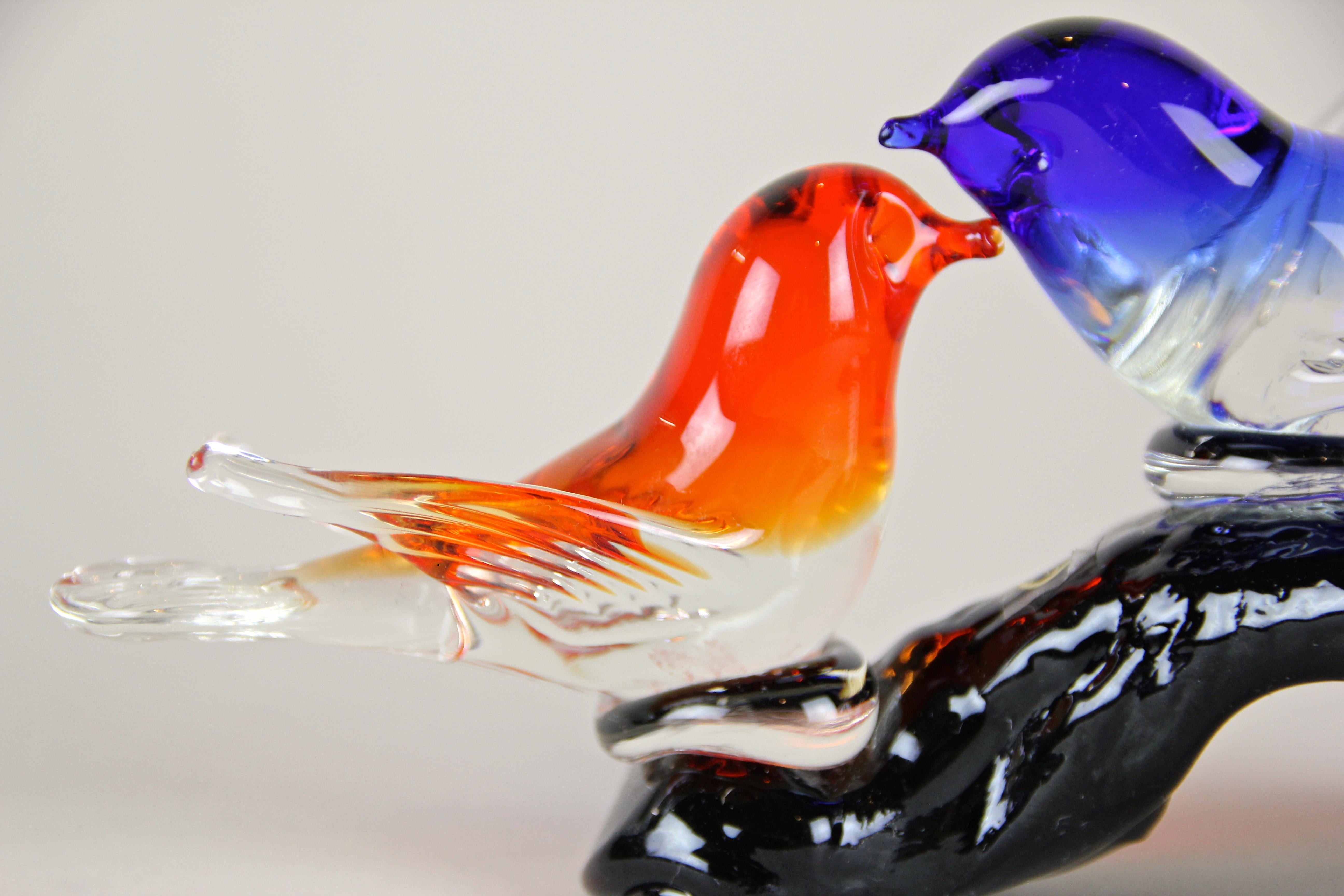 Lovely midcentury Murano glass birds sculpture out of Italy. Coming from the 1960s this small Murano sculpture shows two birds wonderfully designed in shining blue and red tones sitting on a piece of a black branch. A decorative piece of Italian