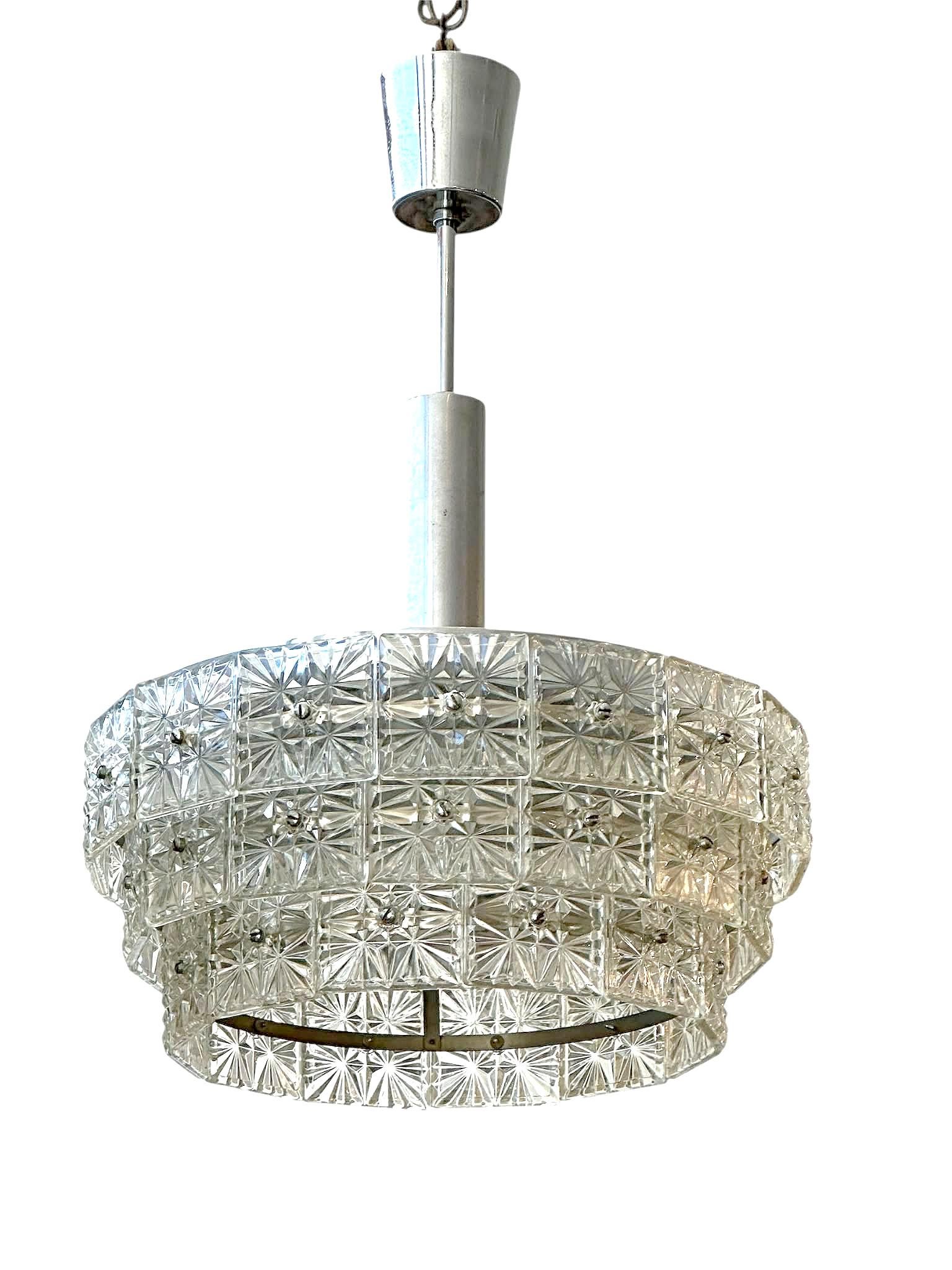 Questo lampadario presenta un design distintivo a gradini con elementi in vetro testurizzato sospesi da una struttura in metallo cromato, esemplificando la sofisticata maestria artigianale e il design innovativo del design italiano del Mid -