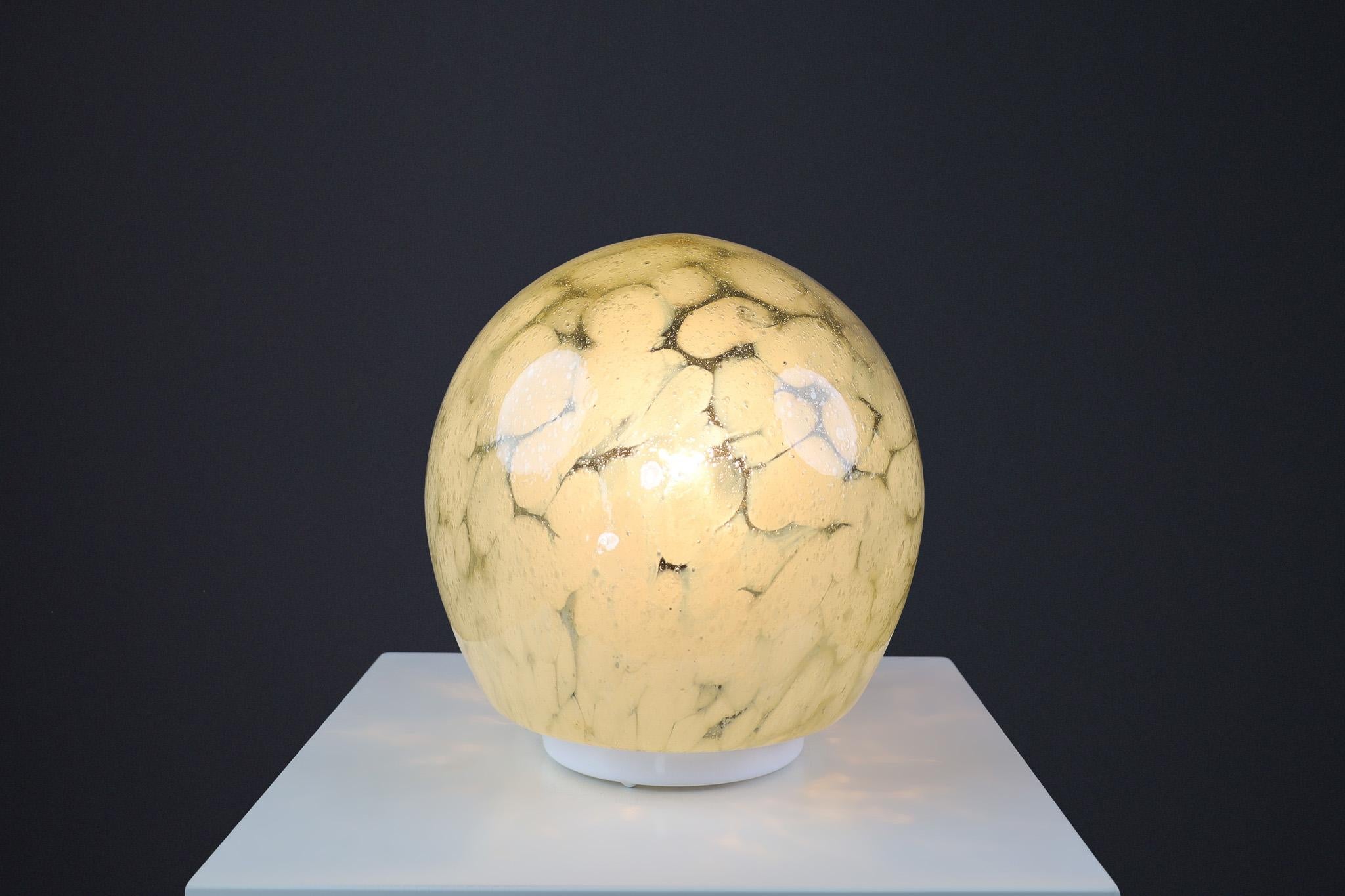 Mid-Century Murano Glass Desk/Table Lamp, Italy 1970s

This 1970s table lamp is crafted from Murano glass in Italy. Its globe-shaped shade and distinct patterns are characteristic of Murano glass from that era. This beautiful piece seamlessly