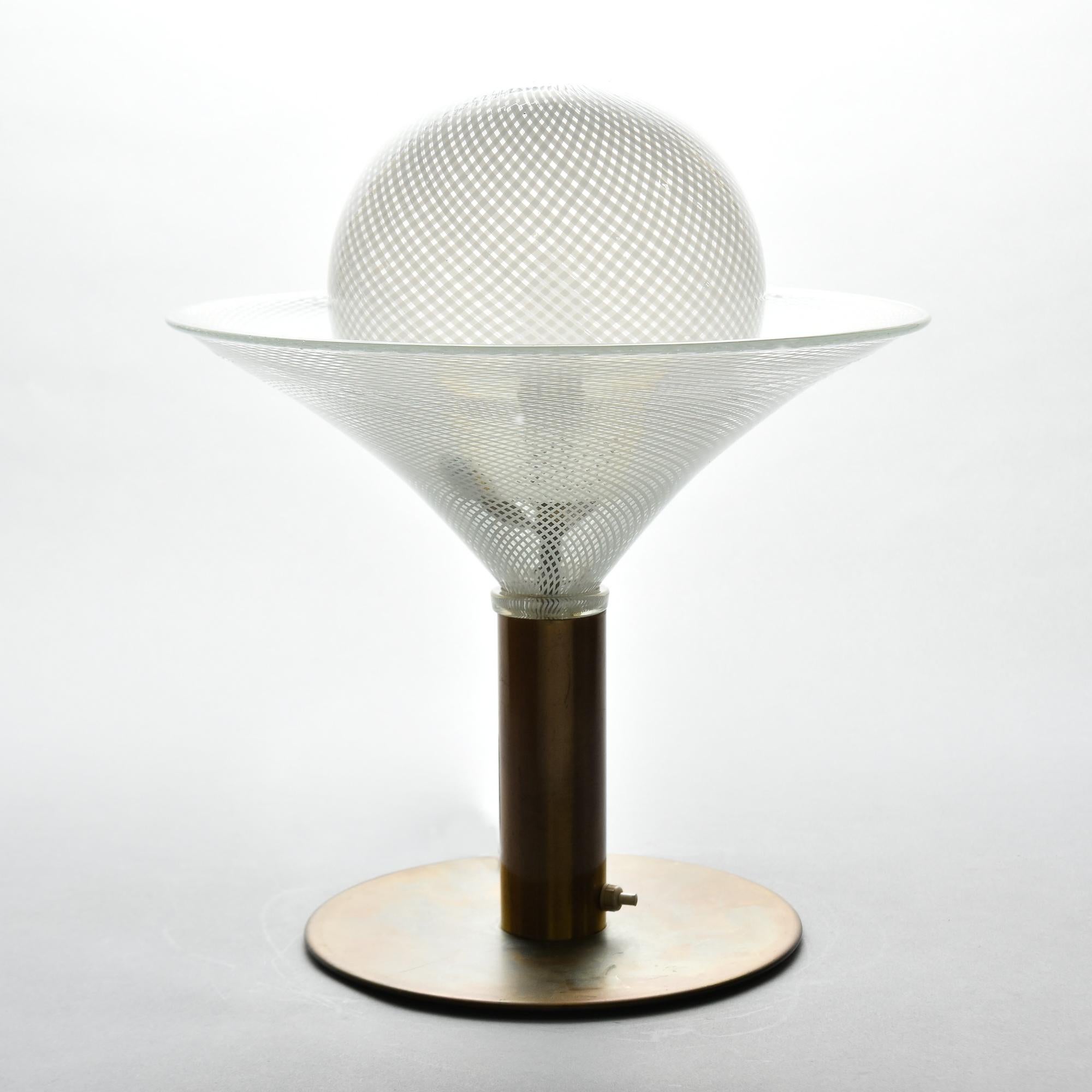 Found in Italy, this circa 1950s Murano glass table lamp has a flat, round brass base with a brass stem that supports a martini-glass-shaped Murano glass base with a mouth blown globe that covers a single light bulb. Glass is clear with a white
