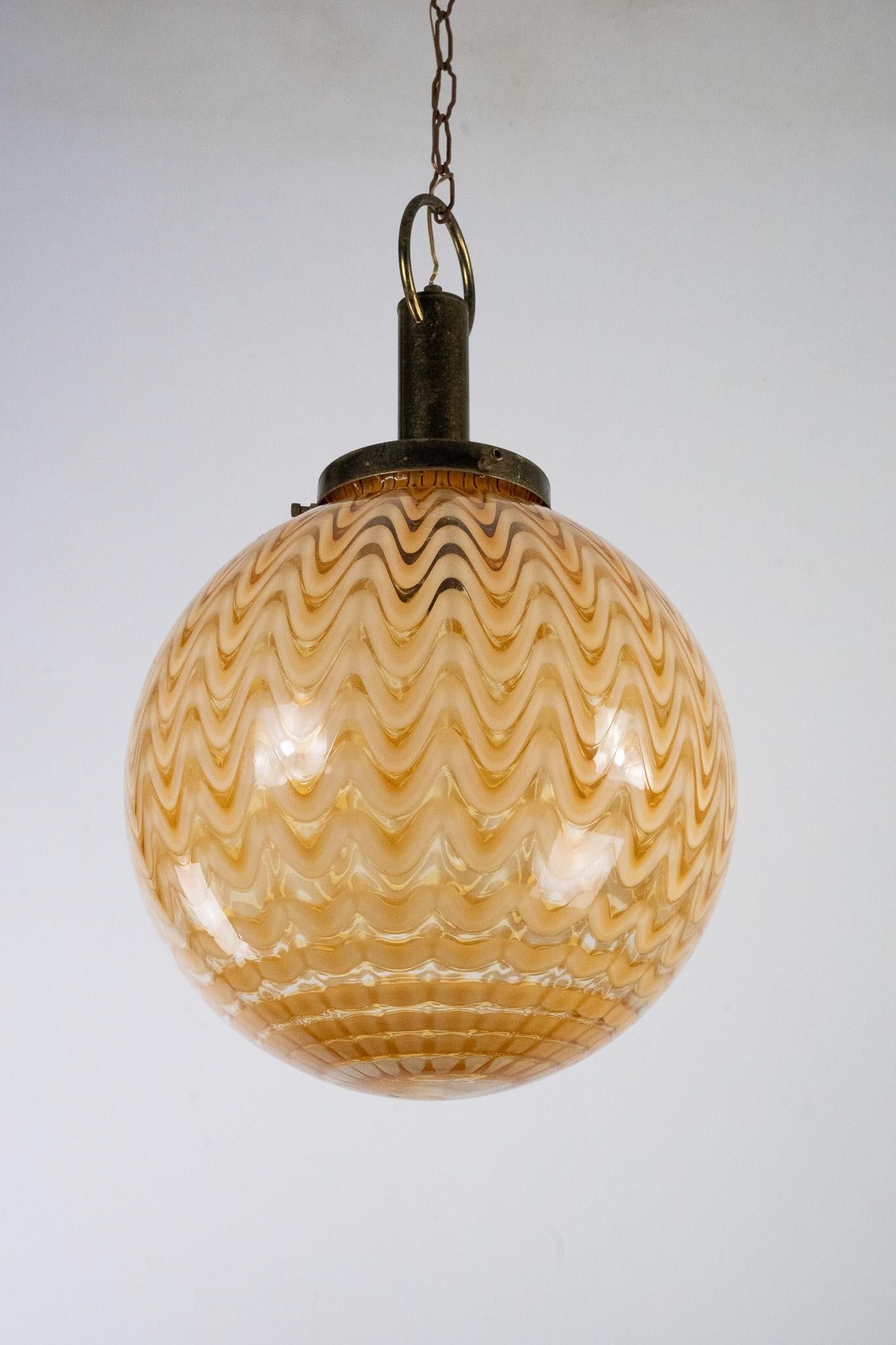 Murano glass sphere chandelier in the style of Venini and produced in Italy during the 70s. The gilded metal part above the sphere has evident trace of age and use with oxidation. The ceiling cup is in good condition with normal signs. The Glass is