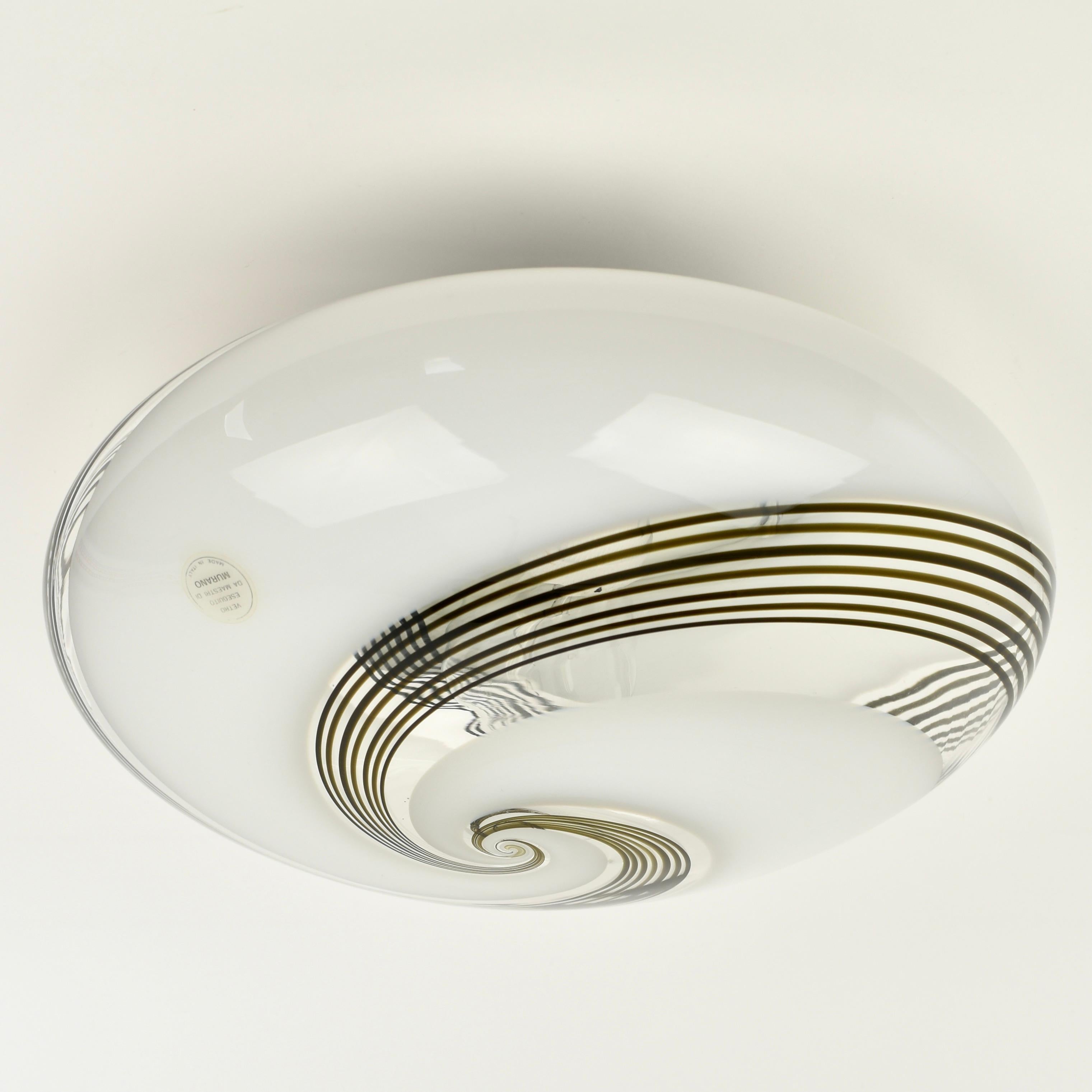 Magnifique encastré en verre tourbillonnant de Murano datant du milieu du siècle dernier. Les rayures sont d'un brun foncé profond, à côté d'un verre blanc et transparent. L'abat-jour a un support en métal blanc et est en bon état vintage.