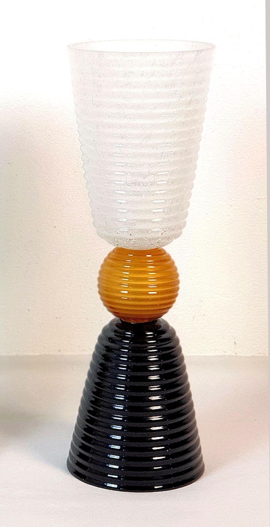 Moderne Murano-Glas-Tischlampe aus der Jahrhundertmitte, Italien 1980er Jahre.
Die italienische Tischlampe ist aus schwarzem und weißem geripptem Murano-Glas gefertigt, mit einer zentralen honigfarbenen Murano-Glaskugel.
Die Glühbirne ist in der
