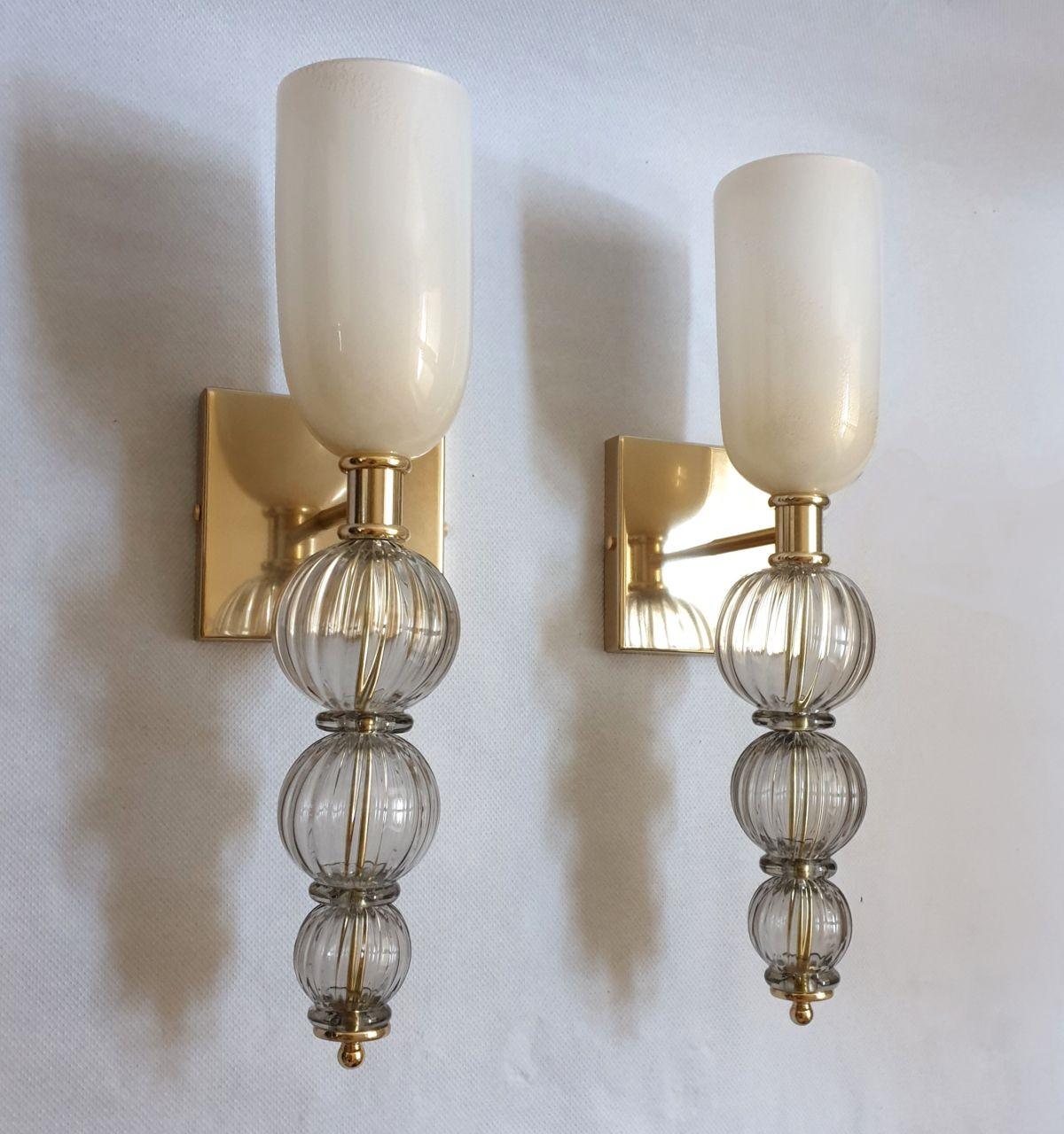 Pair of Mid-Century Modern handblown Murano glass wall sconces, attributed to Venini, Italy 1970s.
The neoclassical sconces have a torchiere shape. 
They are made of a white top vase, nesting the light, with real 24 carrats gold decor;
And three