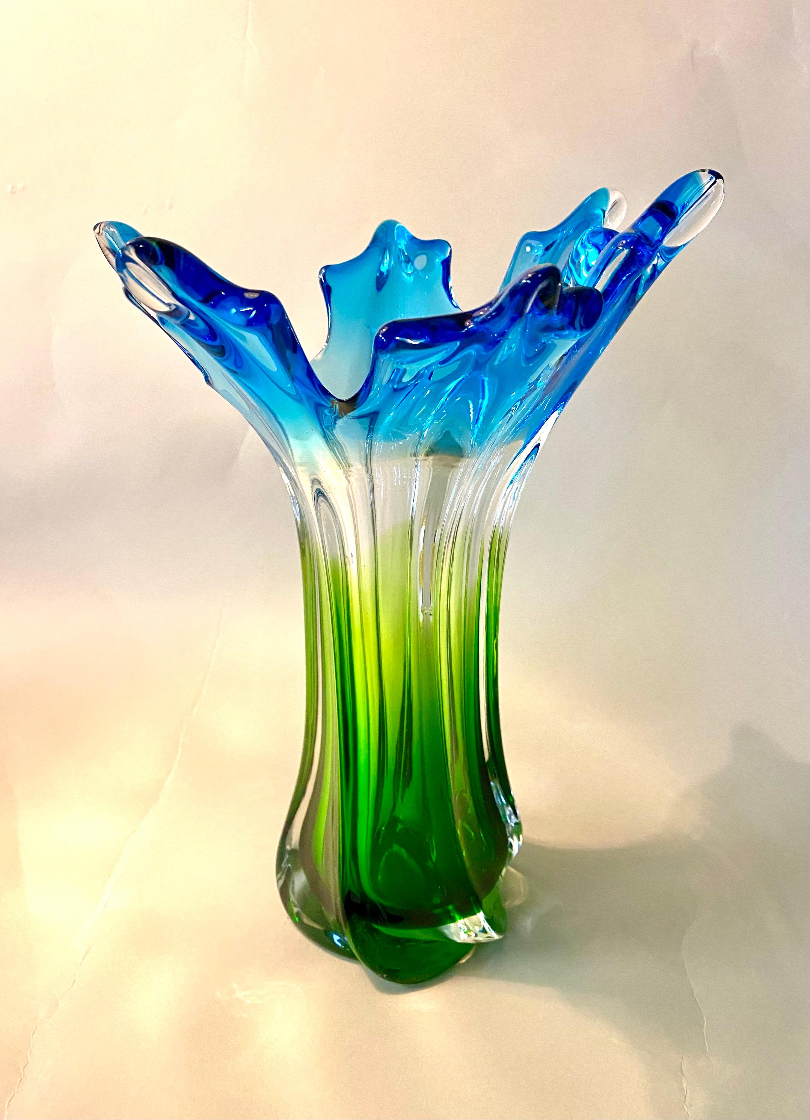 Delicate mid century murano glass vase from the famous workshops in Italy around 1960/70. An extraordinary shaped body combined with an amazing coloration. From different blue tones over clear glass to a beautiful shining green on the base makes