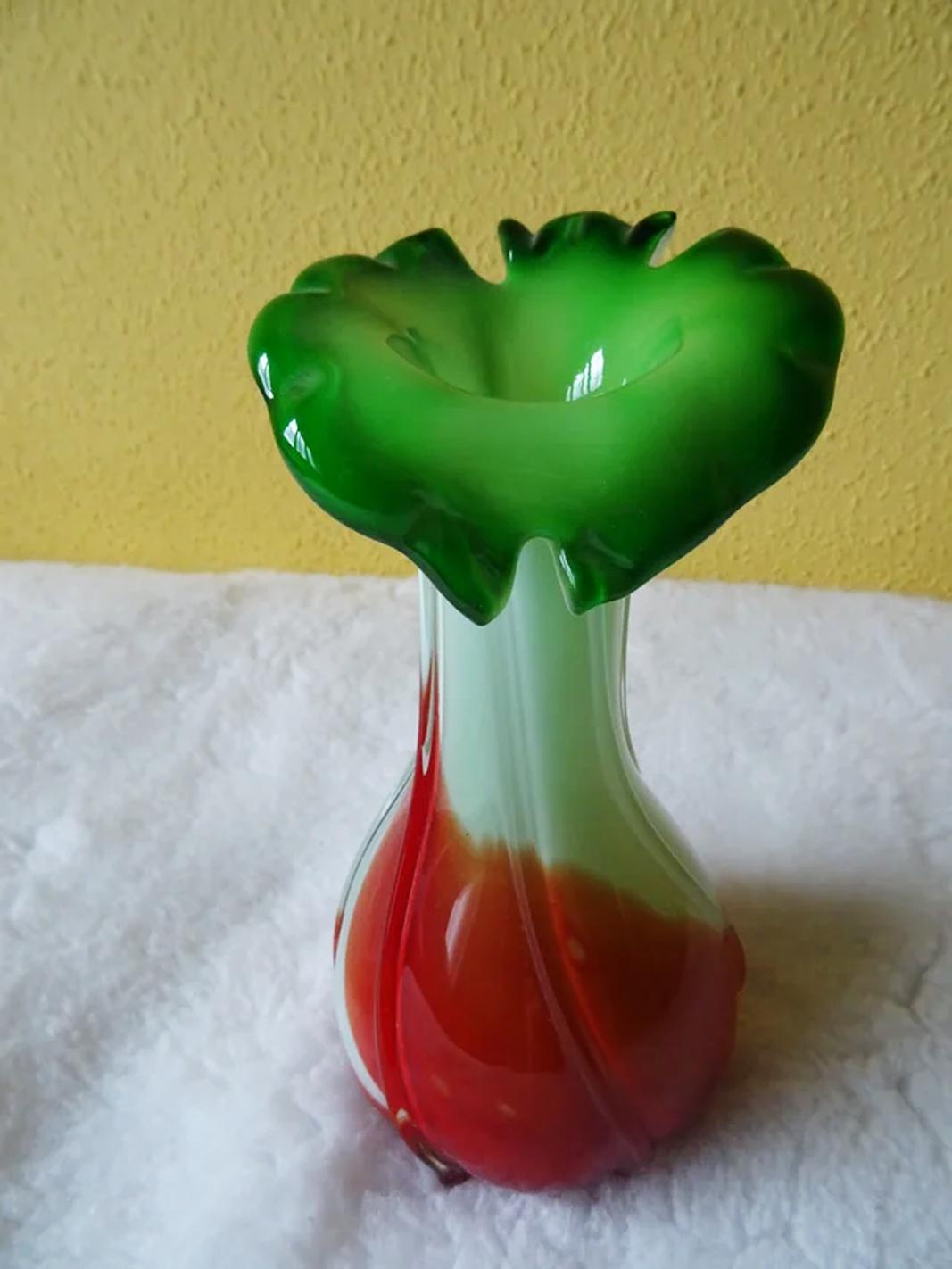 Vase en verre de Murano du milieu du siècle, provenant des célèbres ateliers d'Italie vers 1960/70.
Un corps blanc avec une base rouge et terminé par une sorte de fleur verte
De différentes nuances de blanc, de rouge et de vert. Ce vase en verre