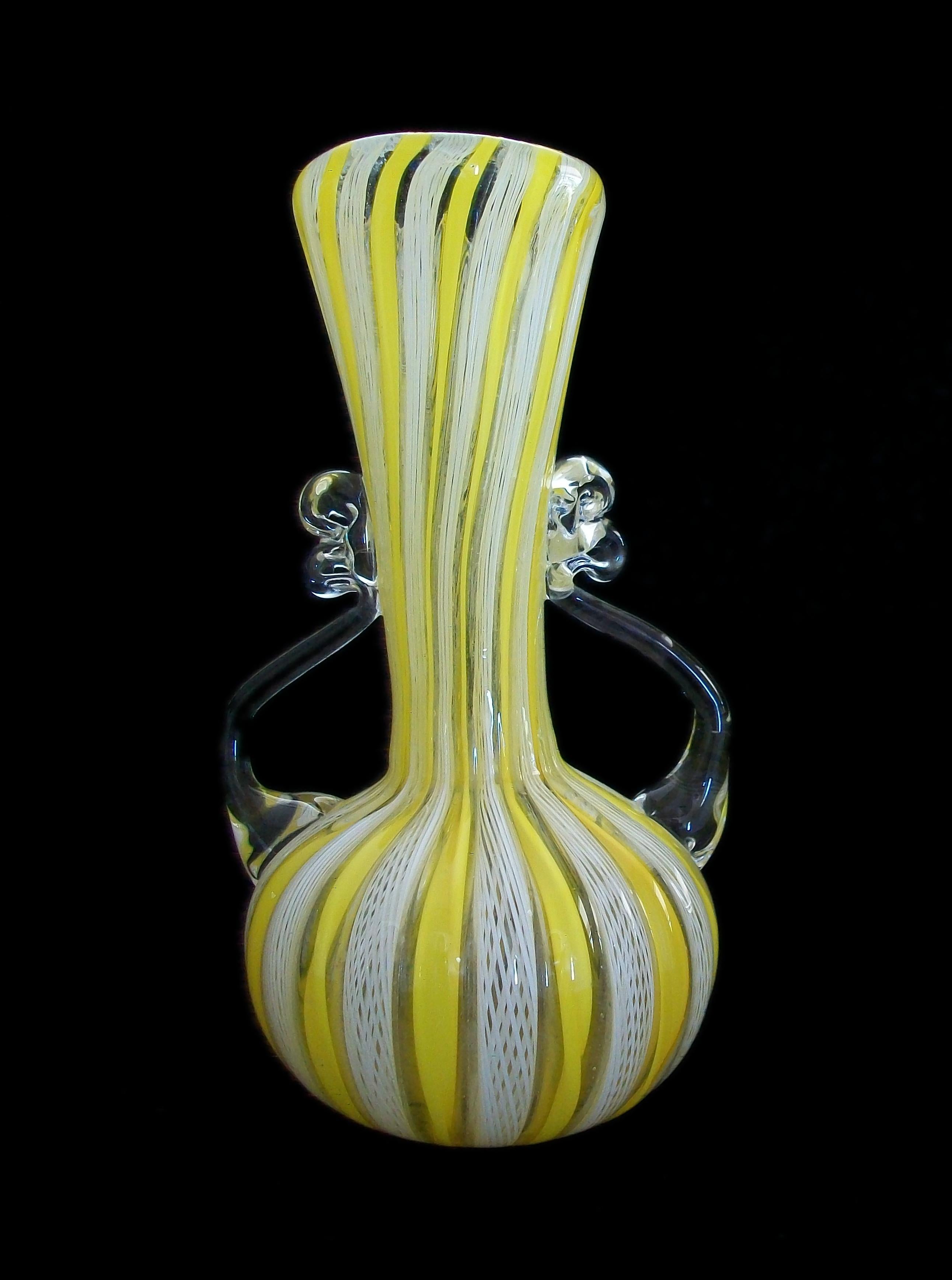 Vase en verre Latticino de Murano, datant du milieu du siècle dernier - deux anses en verre transparent - petit format d'armoire - base polie semi lisse - non signé - Italie - circa 1960's.

Excellent/neutre état vintage - rayures mineures à la